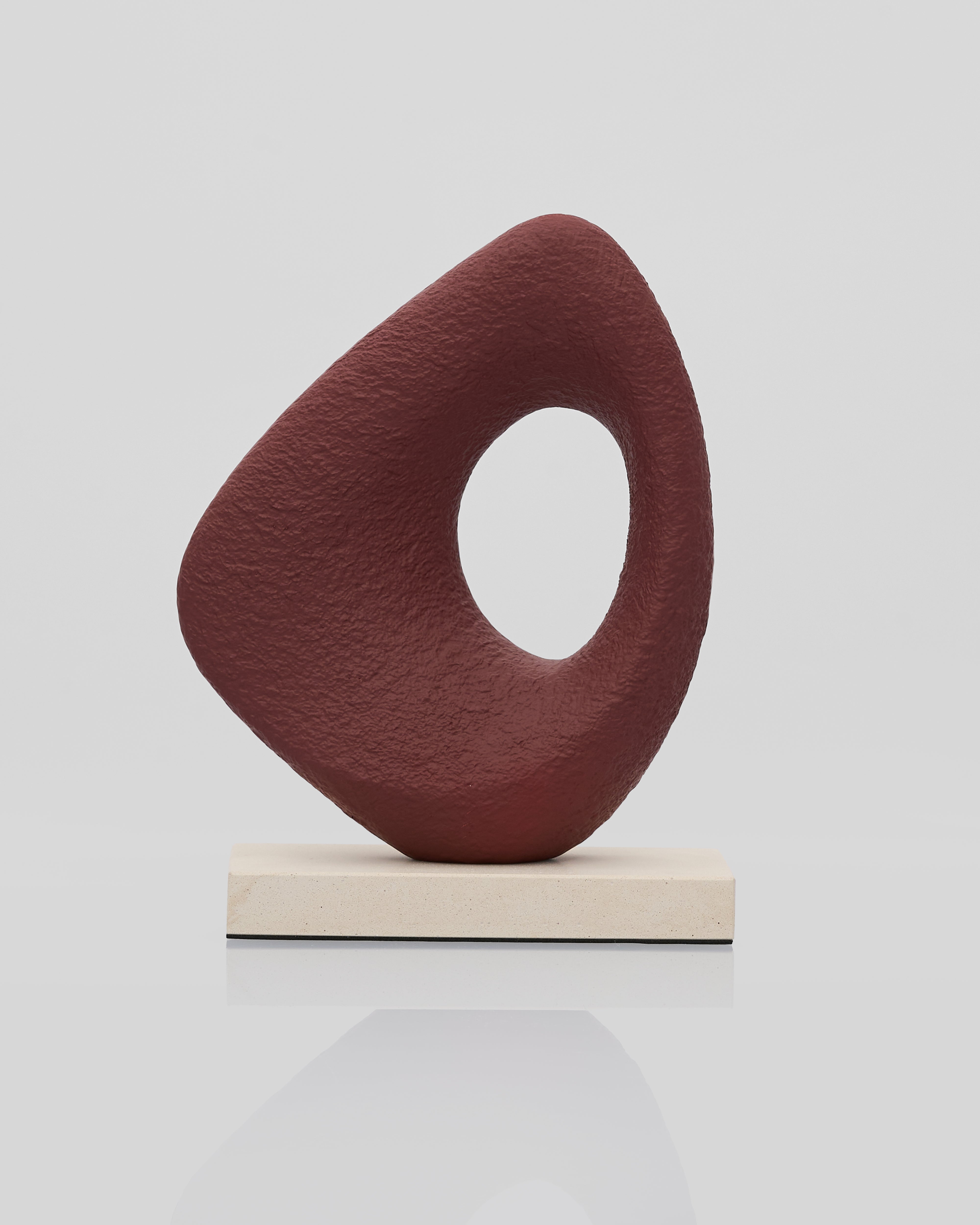 Maroon abstract sculpture on a white platform with a light gray background