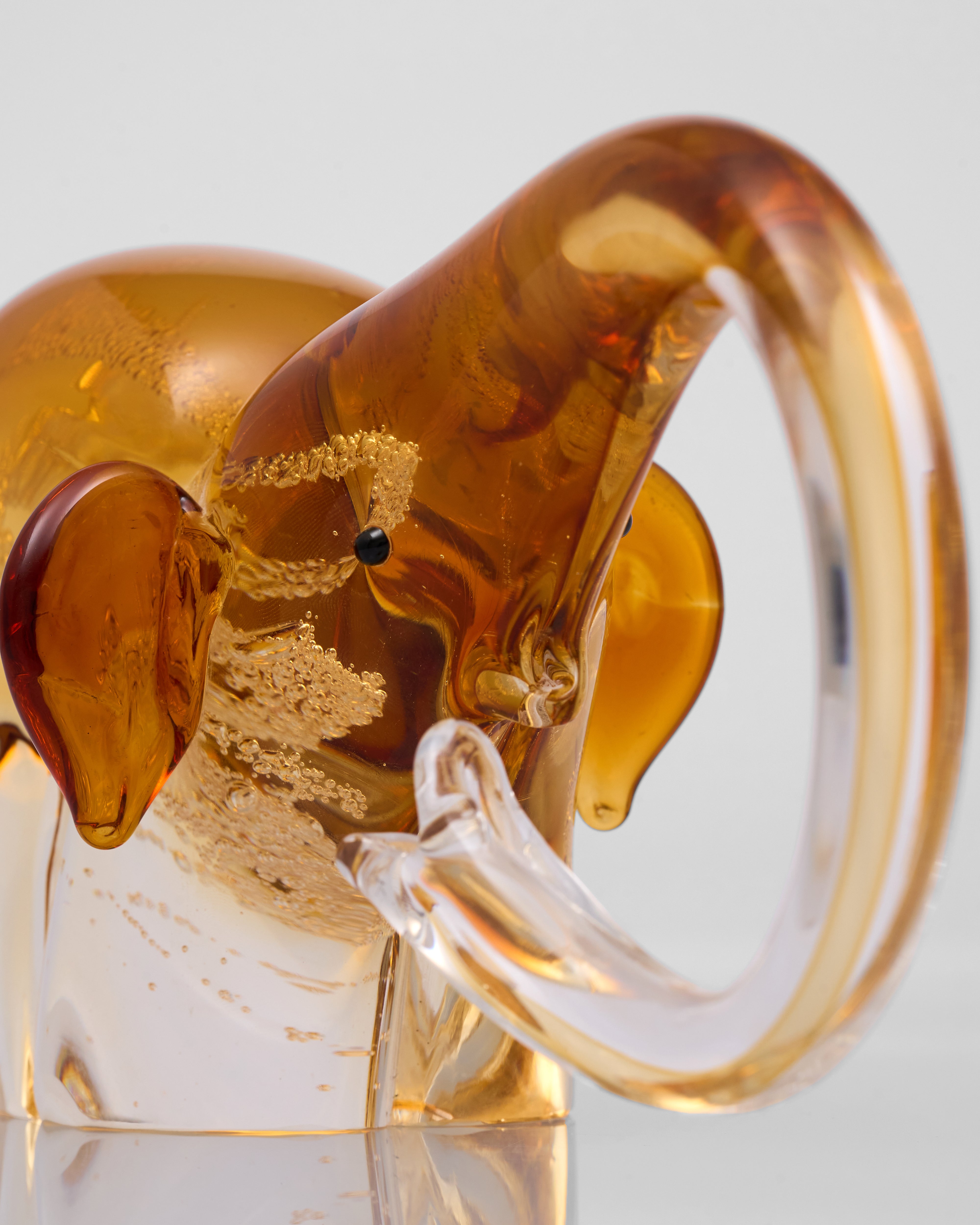 Glass elephant figurine with amber-colored trunk on a reflective surface