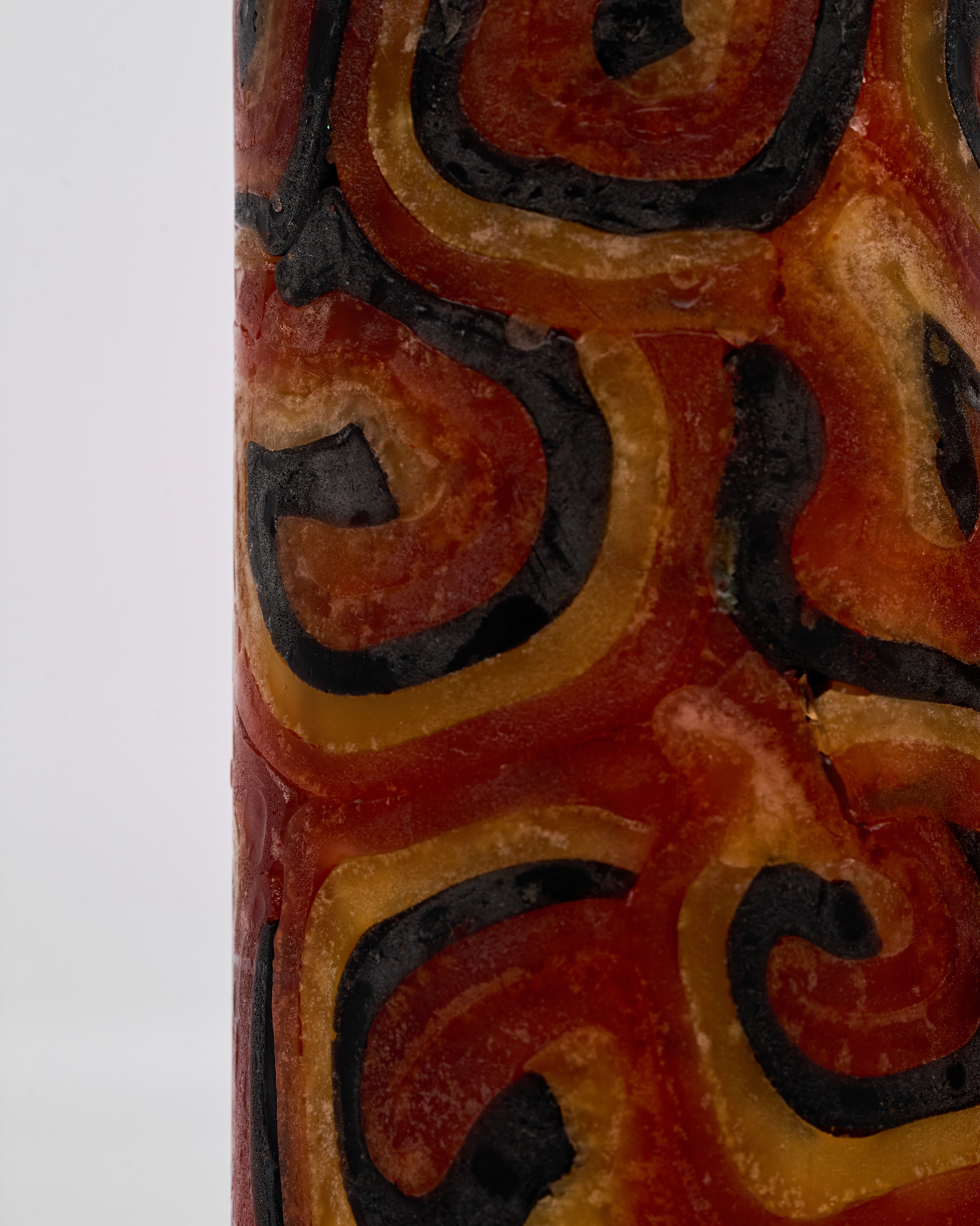 Close-up of a decorative candle red with swirling patterns in red, orange, and black on a white background.