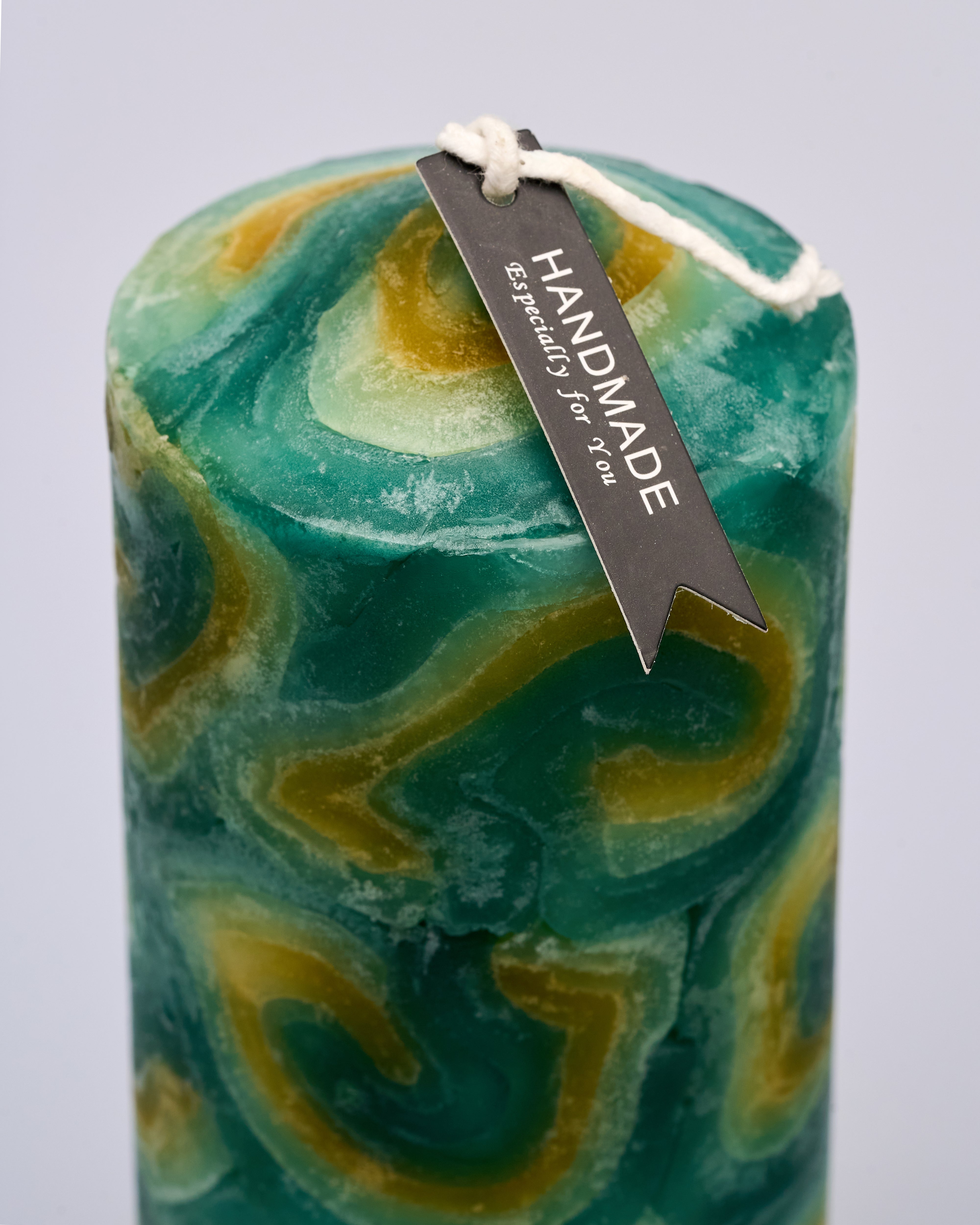 Marbled green and gold candle with a 'Handmade' tag on a light gray background