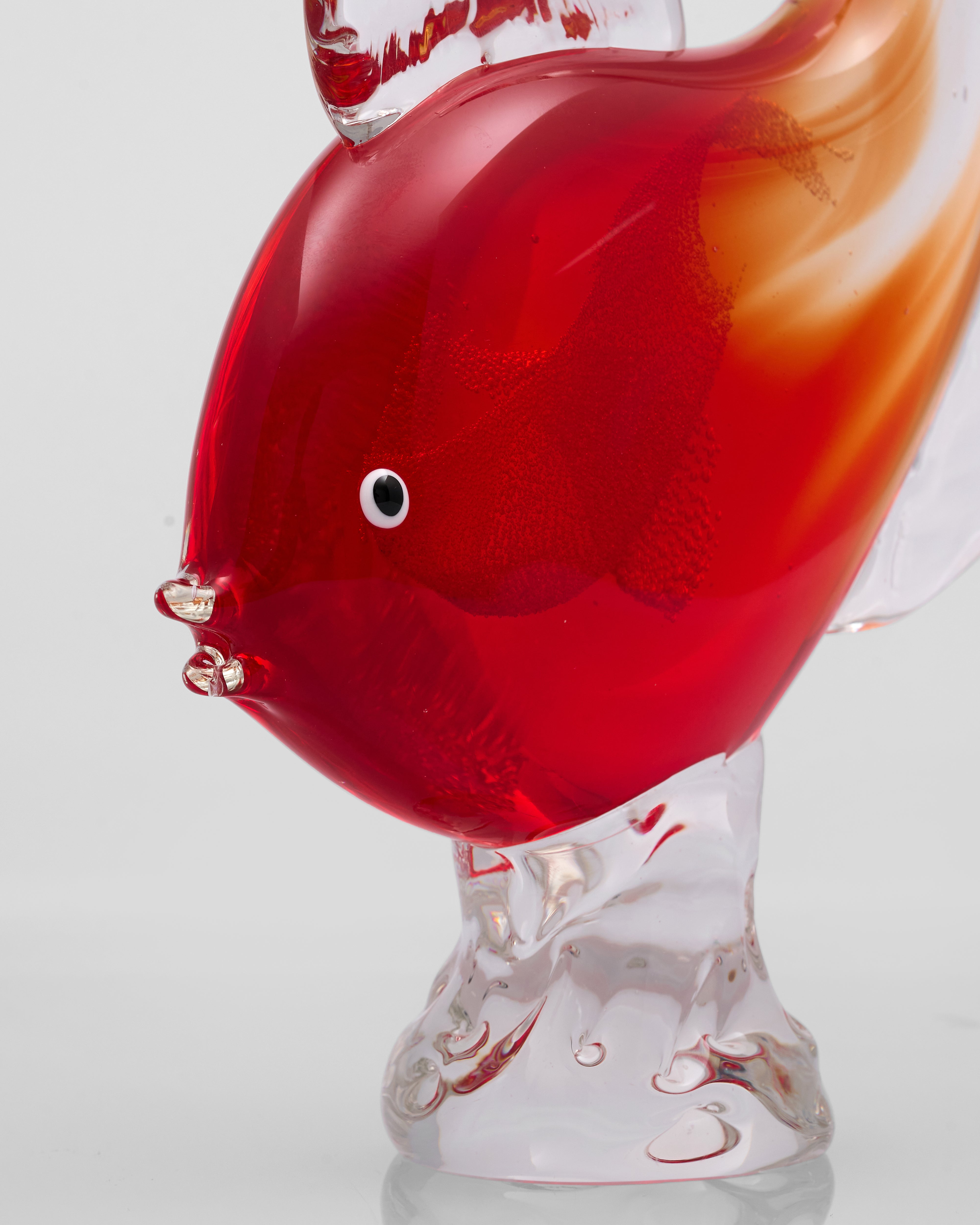 Glass sculpture of a red and orange fish on a white background