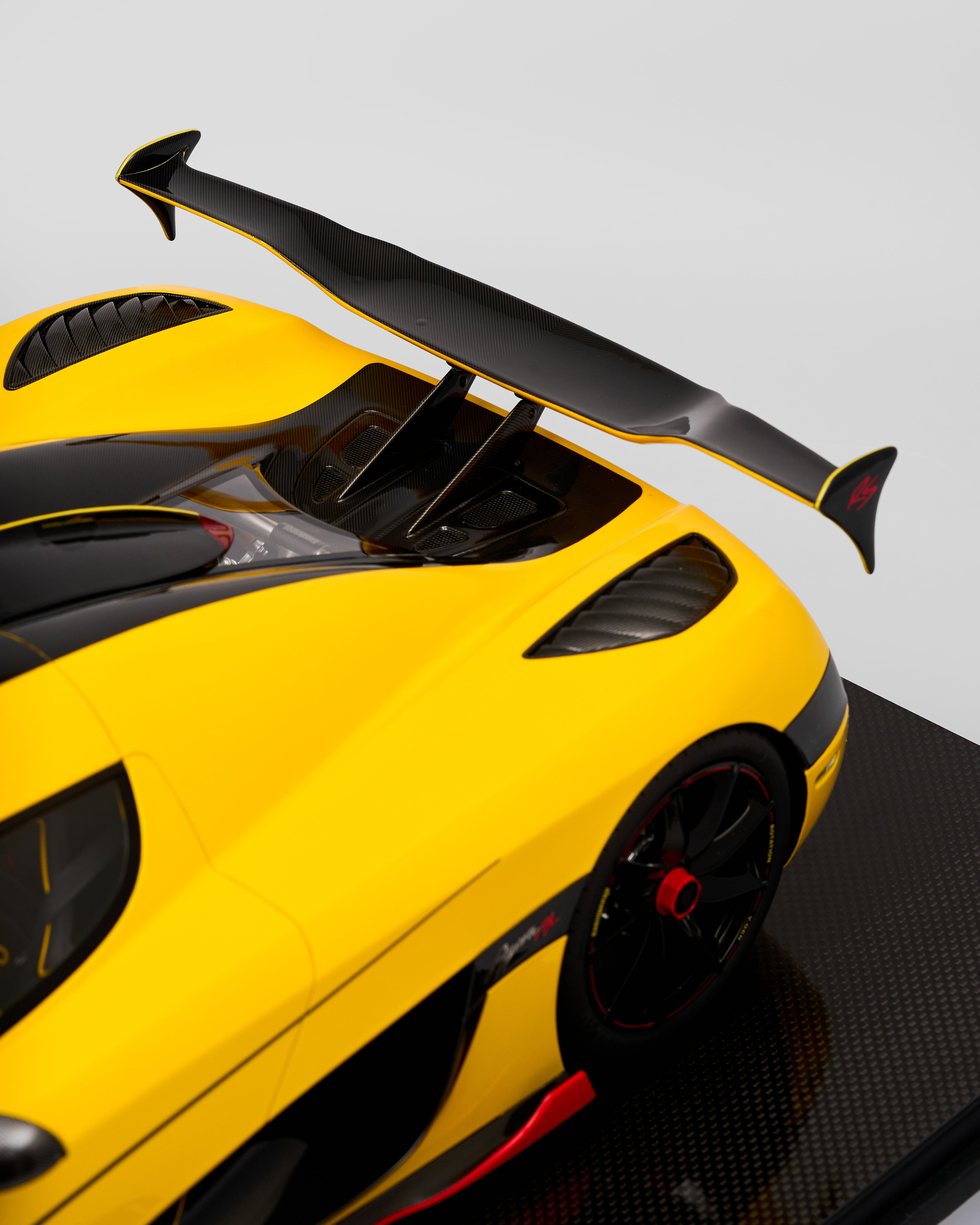 Yellow sports car with a large black rear wing and spoiler on a gray background