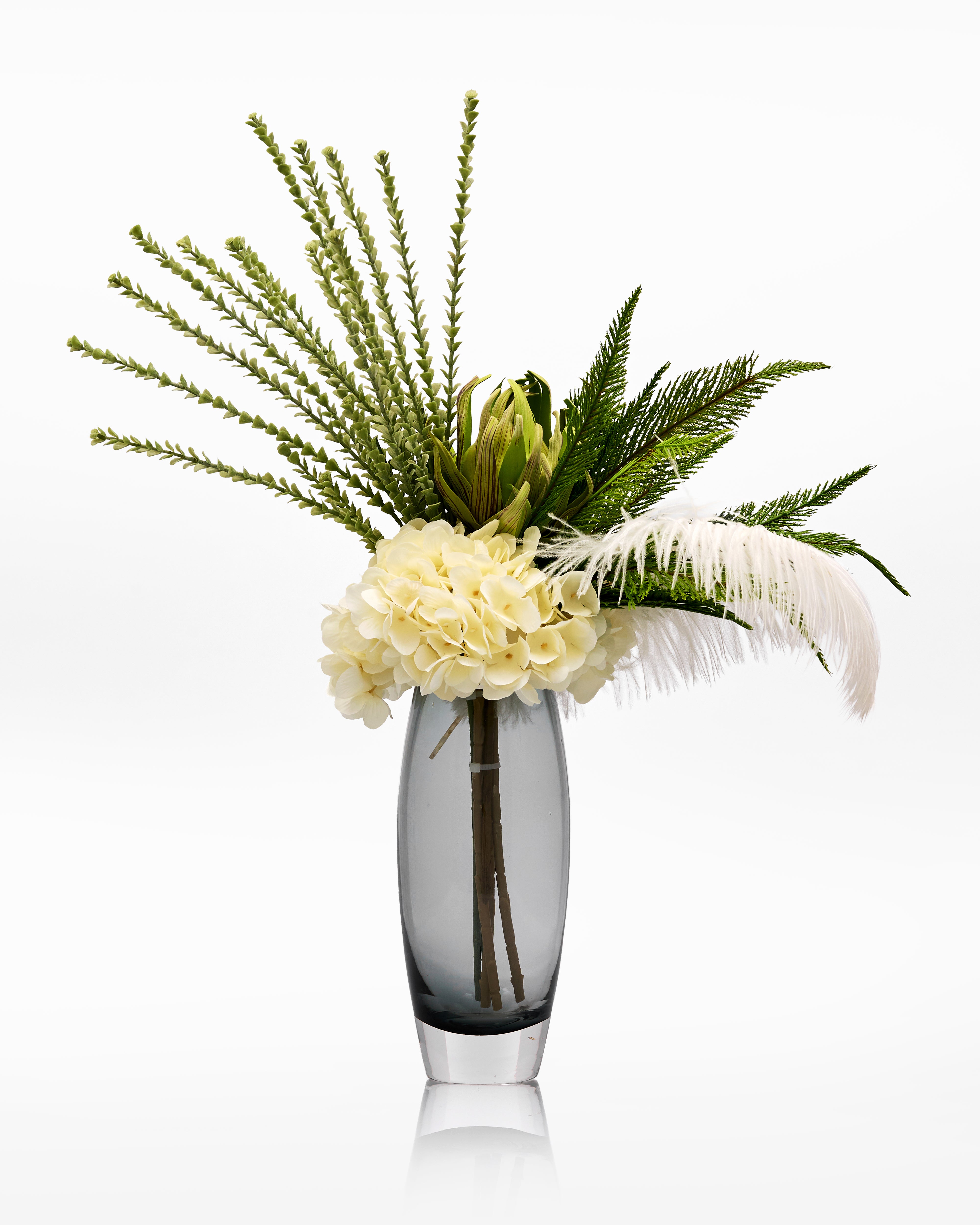Decorative floral arrangement with greenery and white flowers in a clear vase on a white background