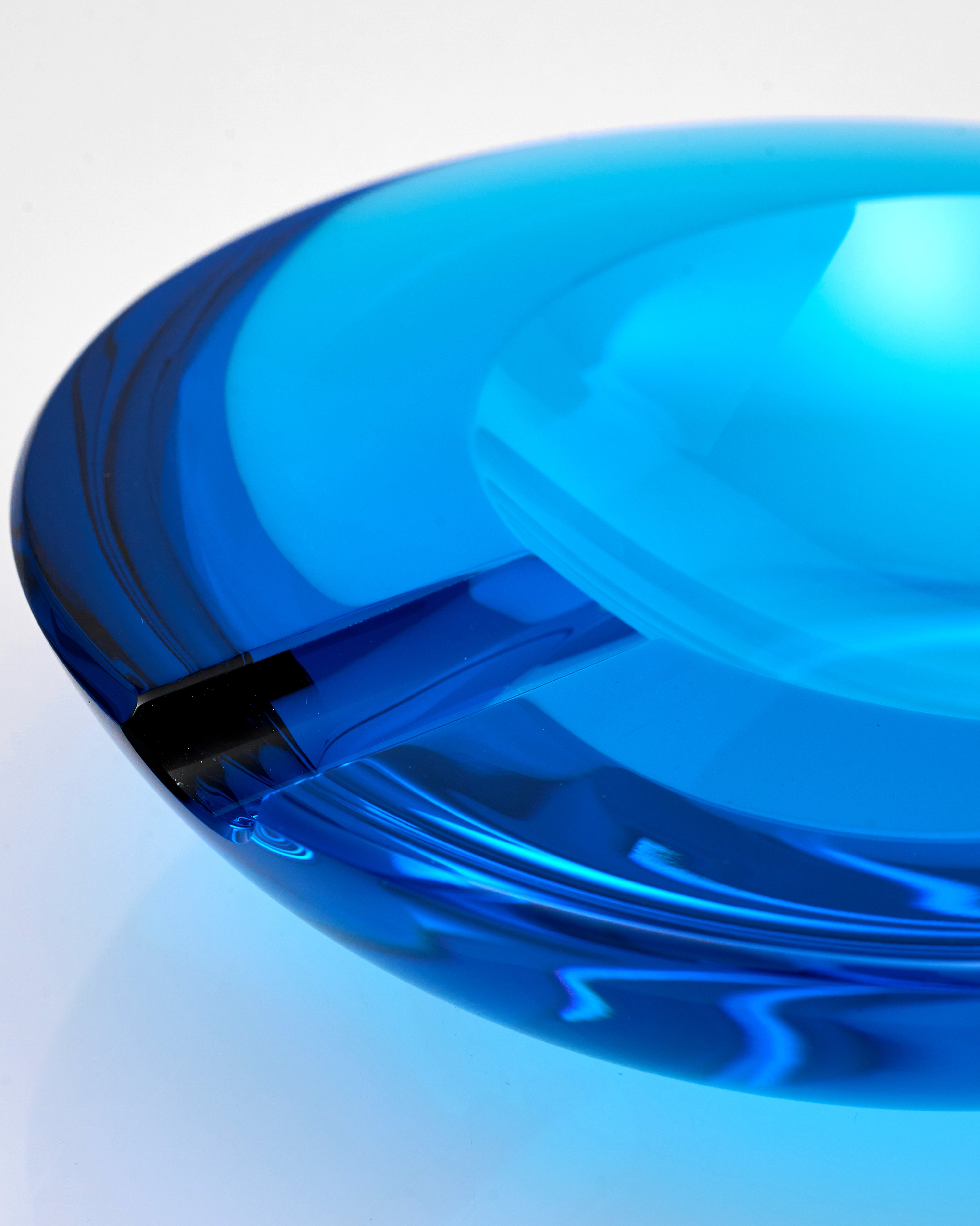 Close-up of a blue glass ashtray with a white interior on a light gray background