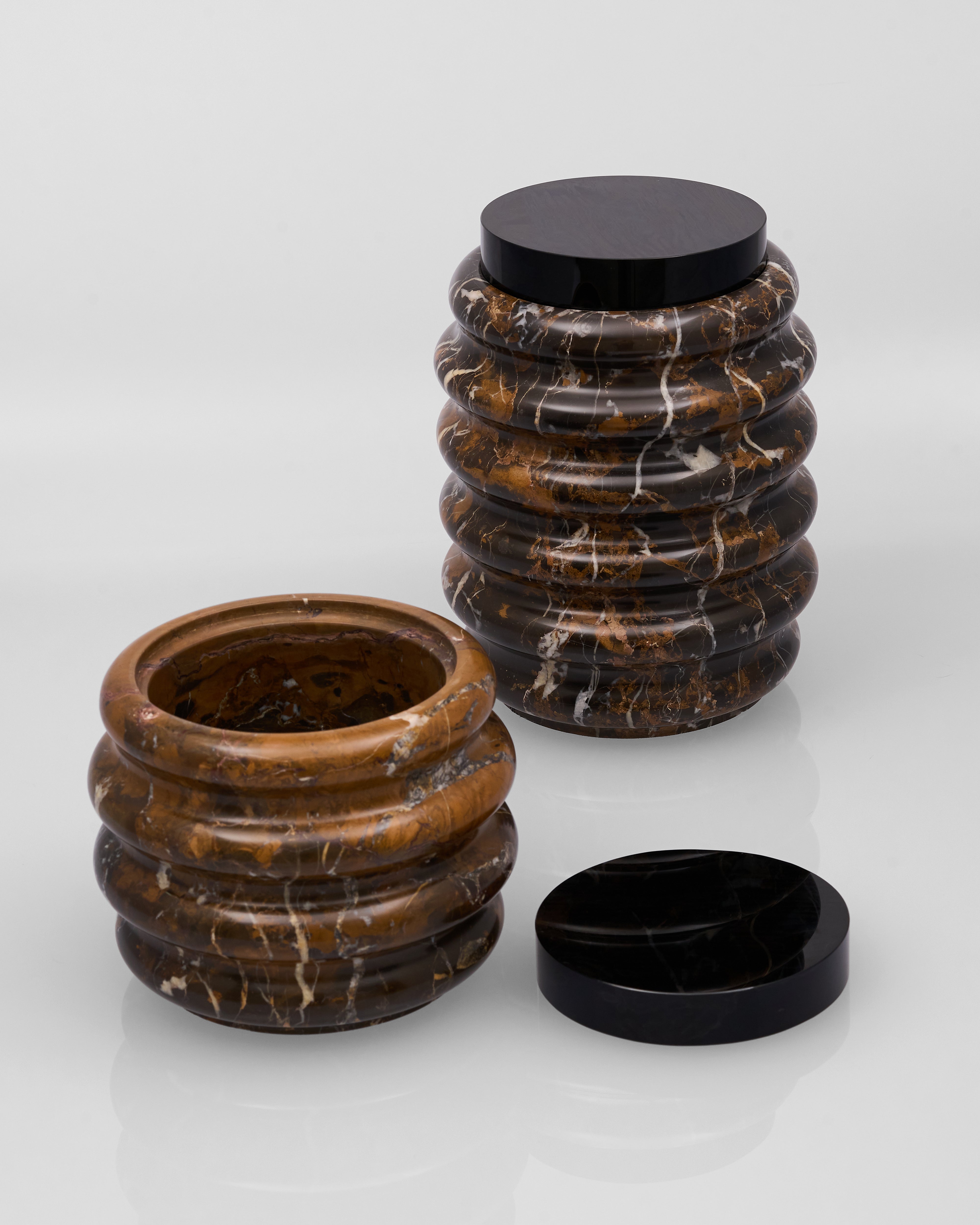 Two marble containers with ribbed design and black lids on a white background