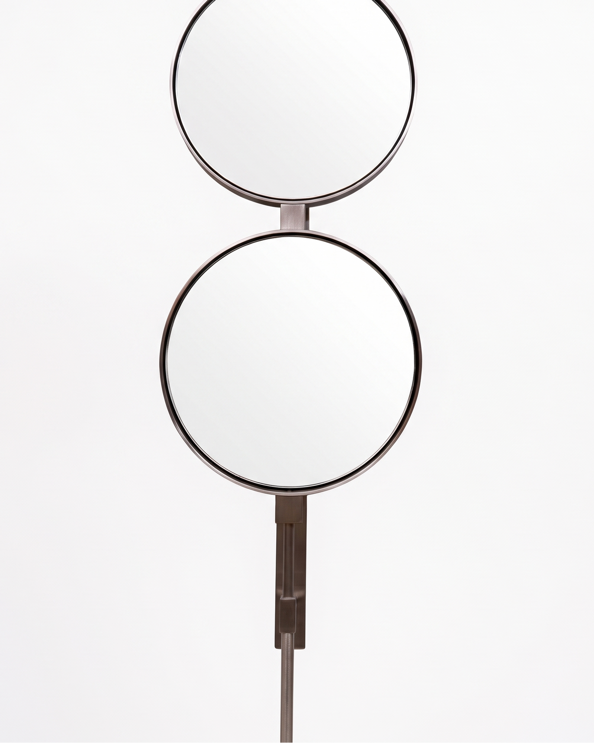 A modern double-height wall mirror with two circular reflective surfaces connected by a slim central stem, finished in a dark metallic bronze tone, shown against a plain white background.