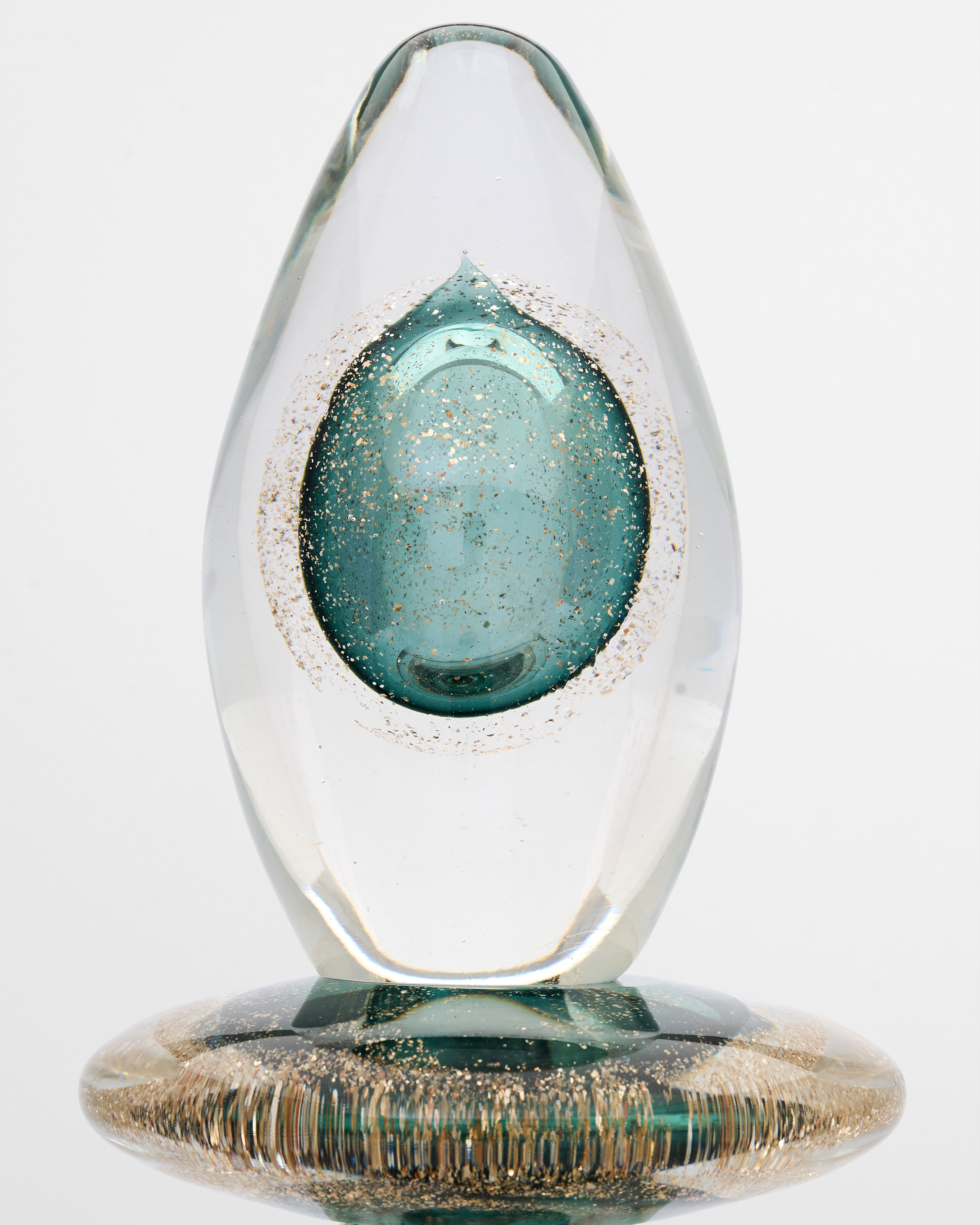 Glass teardrop sculpture with a blue center and gold base on a white background