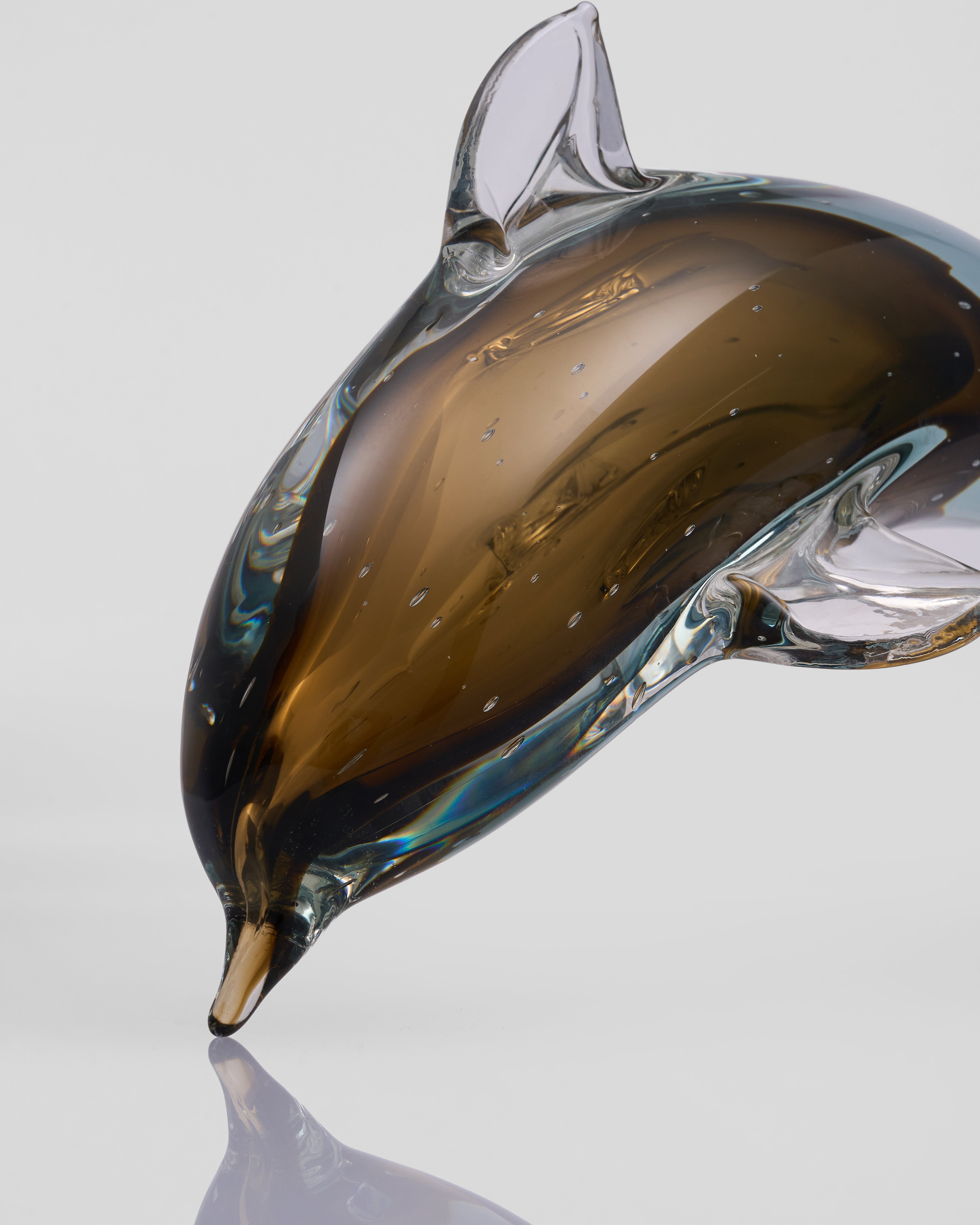 Glass dolphin sculpture on a reflective surface with a light gray background
