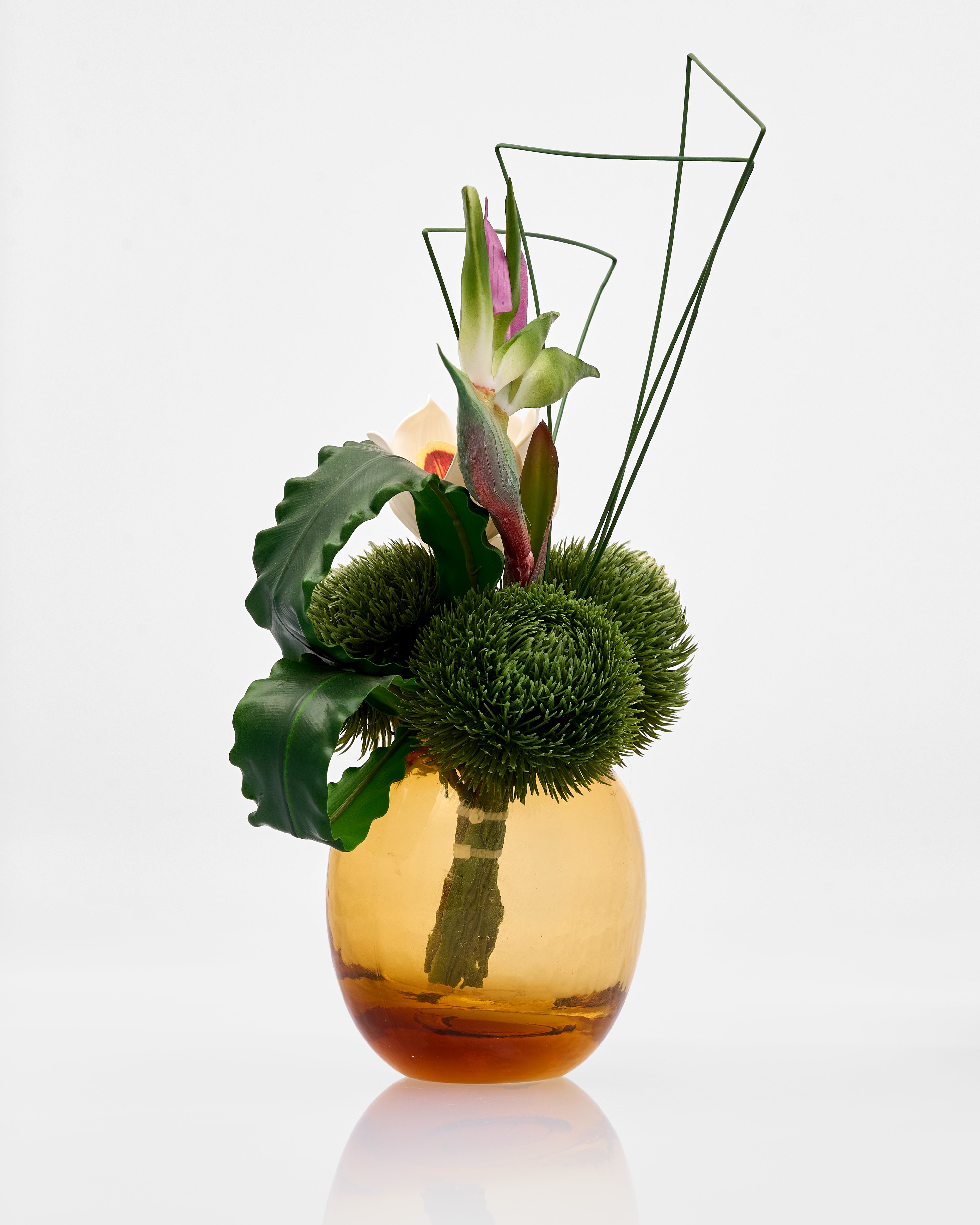 Decorative flower arrangement in a glass vase on a reflective surface with a white background