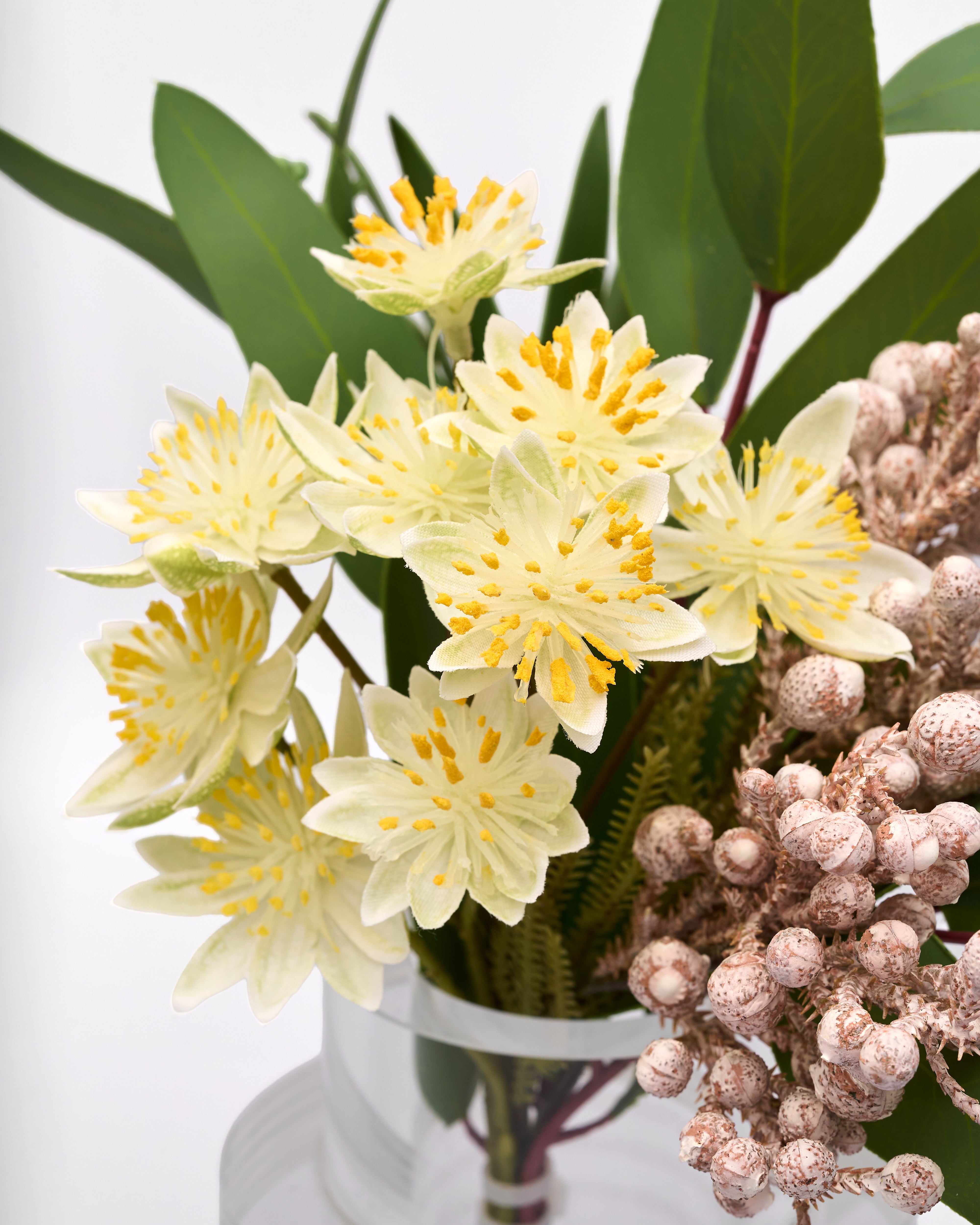 Bouquet of yellow flowers with green leaves and pinkish-brown berries in a clear vase.