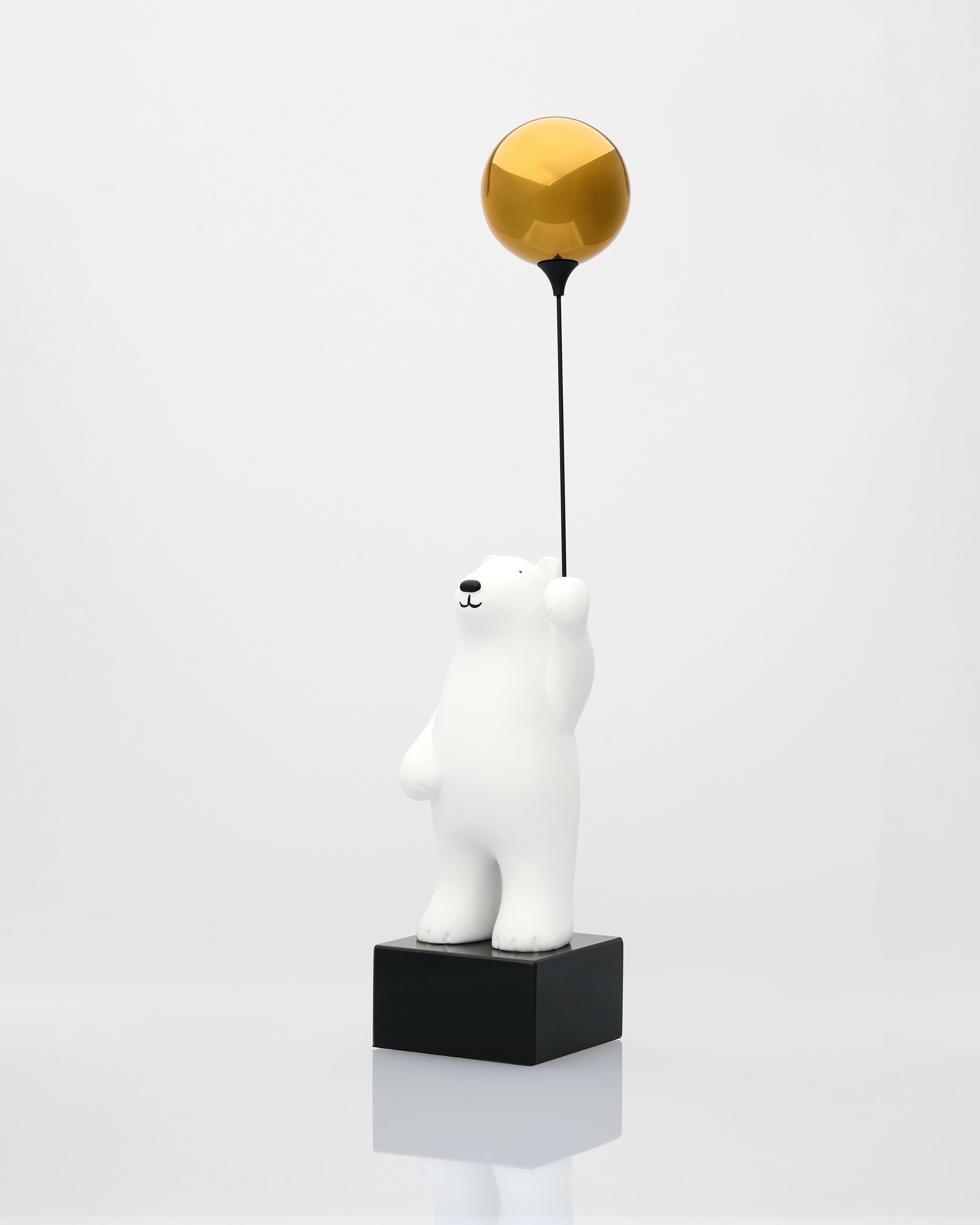 White polar bear figurine with a gold ball on a black stand against a white background