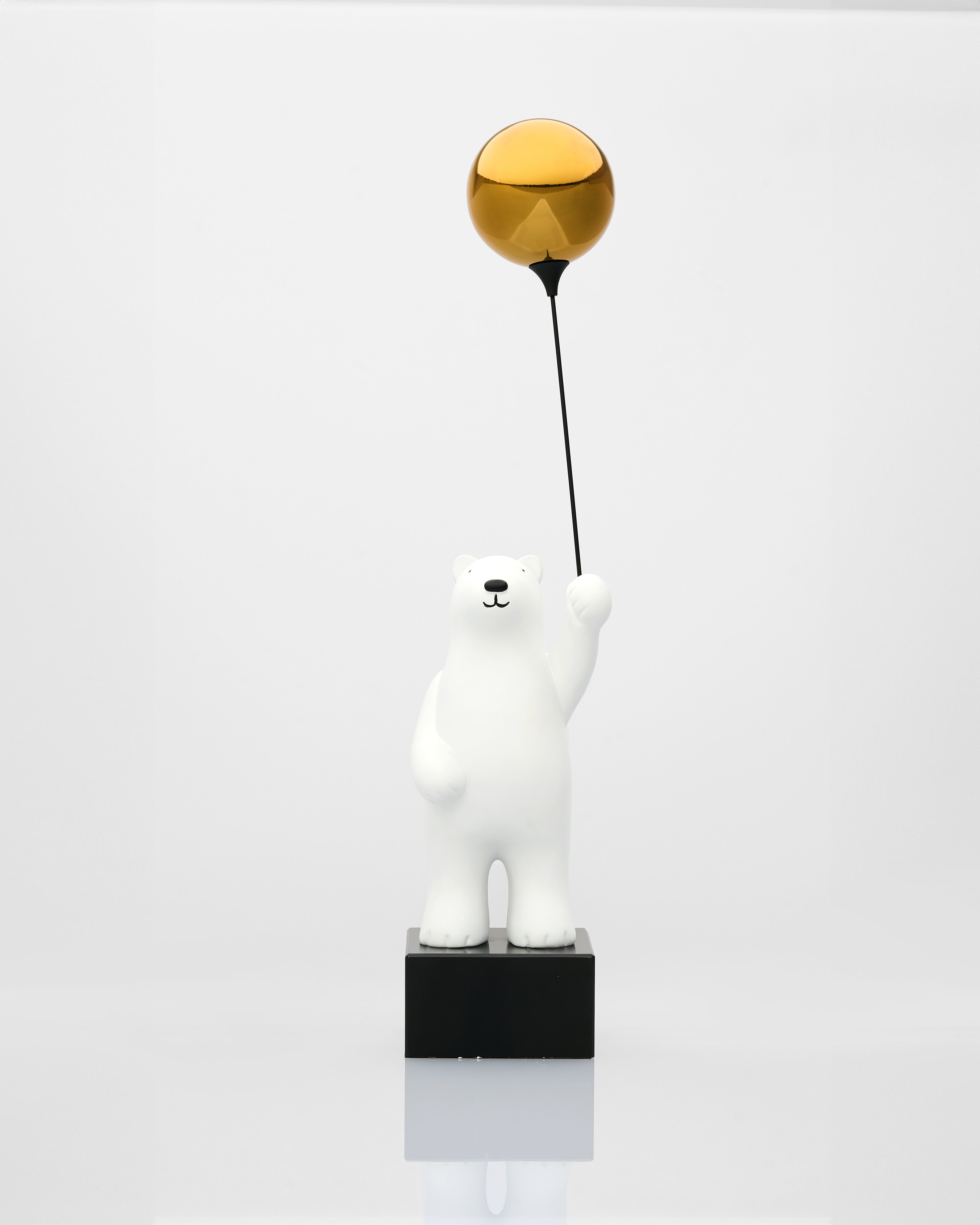 Polar bear figurine holding a gold ball on a white background