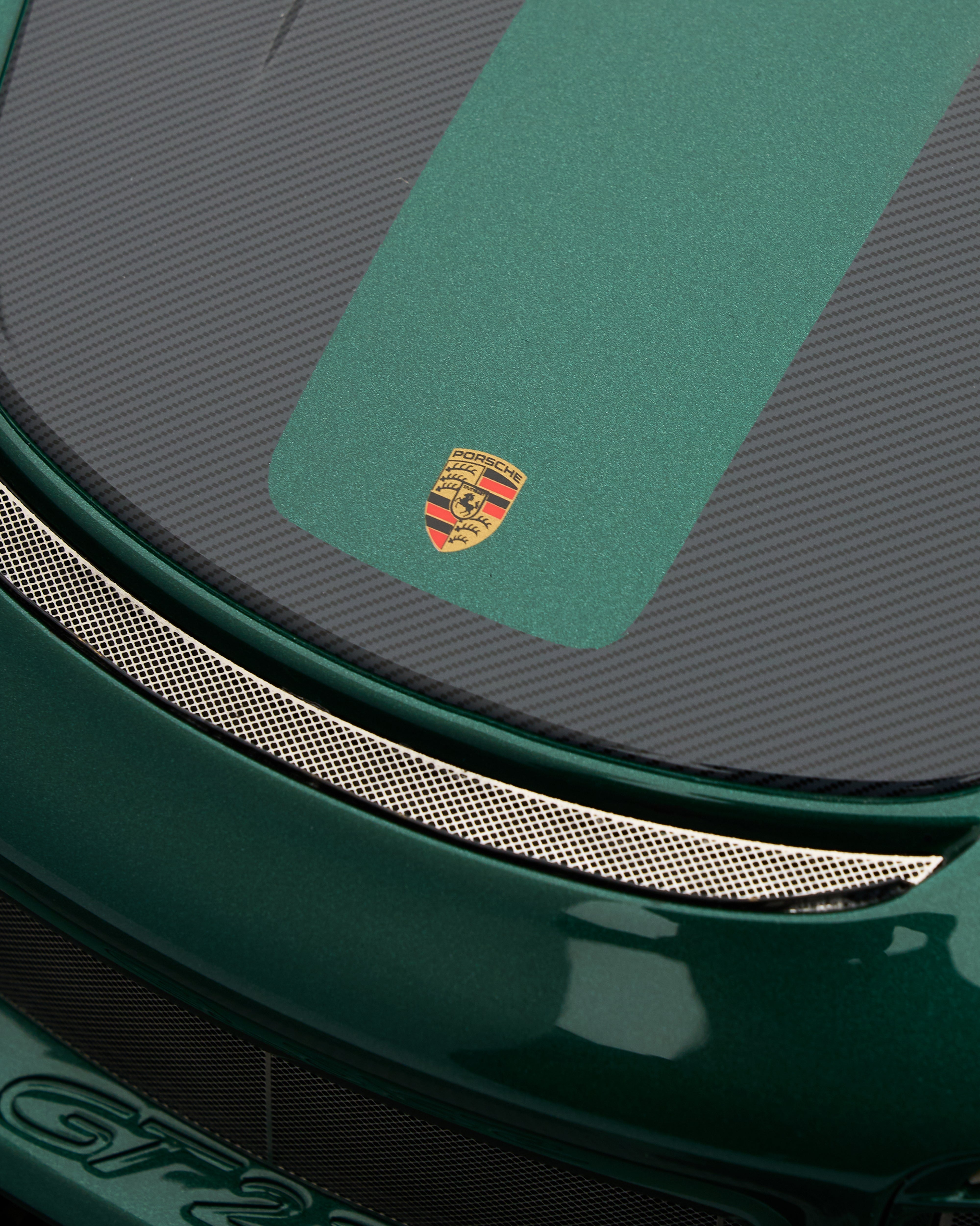 Close-up of a green car with a Porsche logo on the hood