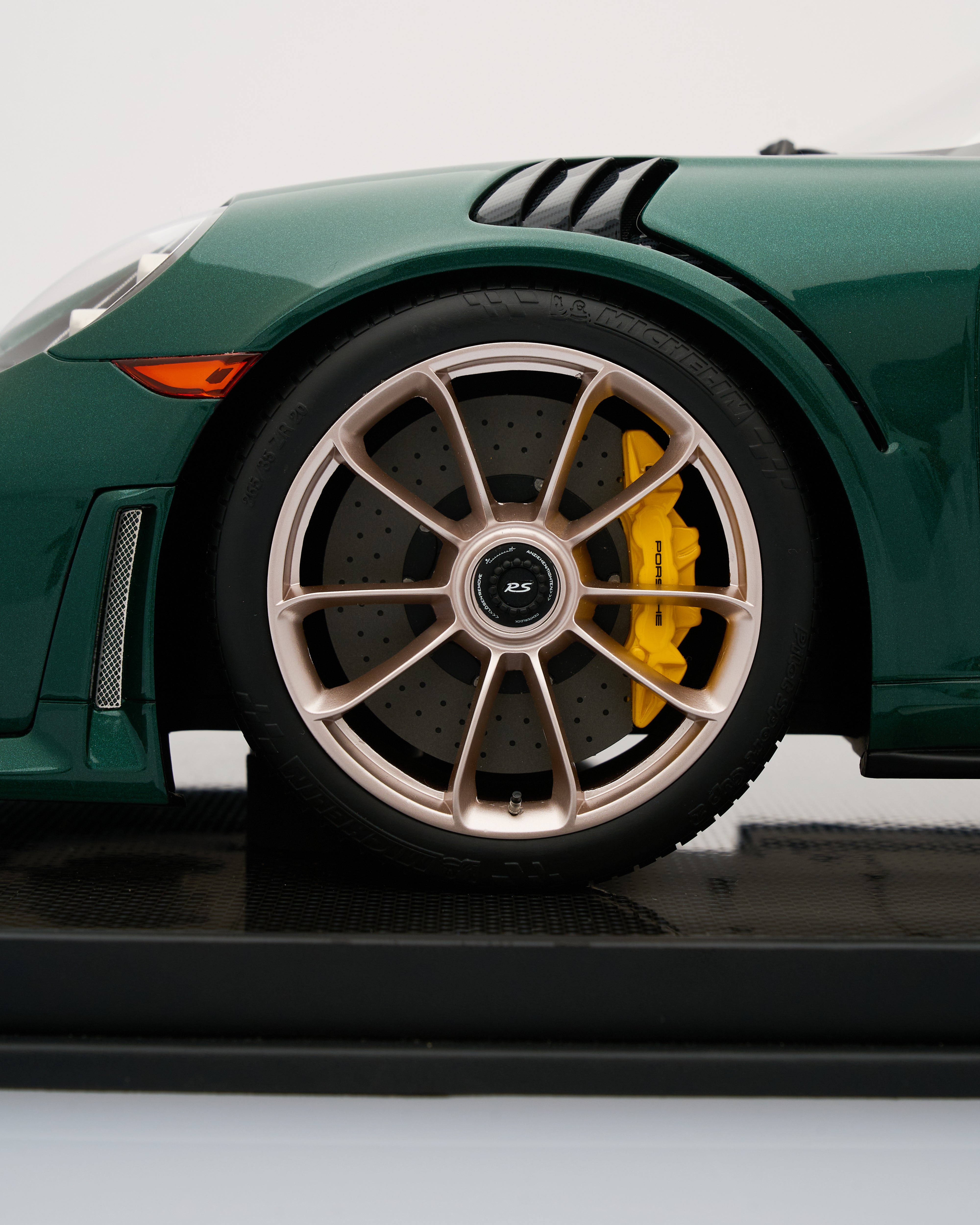 Close-up of a Porsche 911 GT2RS Irish Green sports car scale model wheel with a gold rim and yellow brake caliper on a white background.