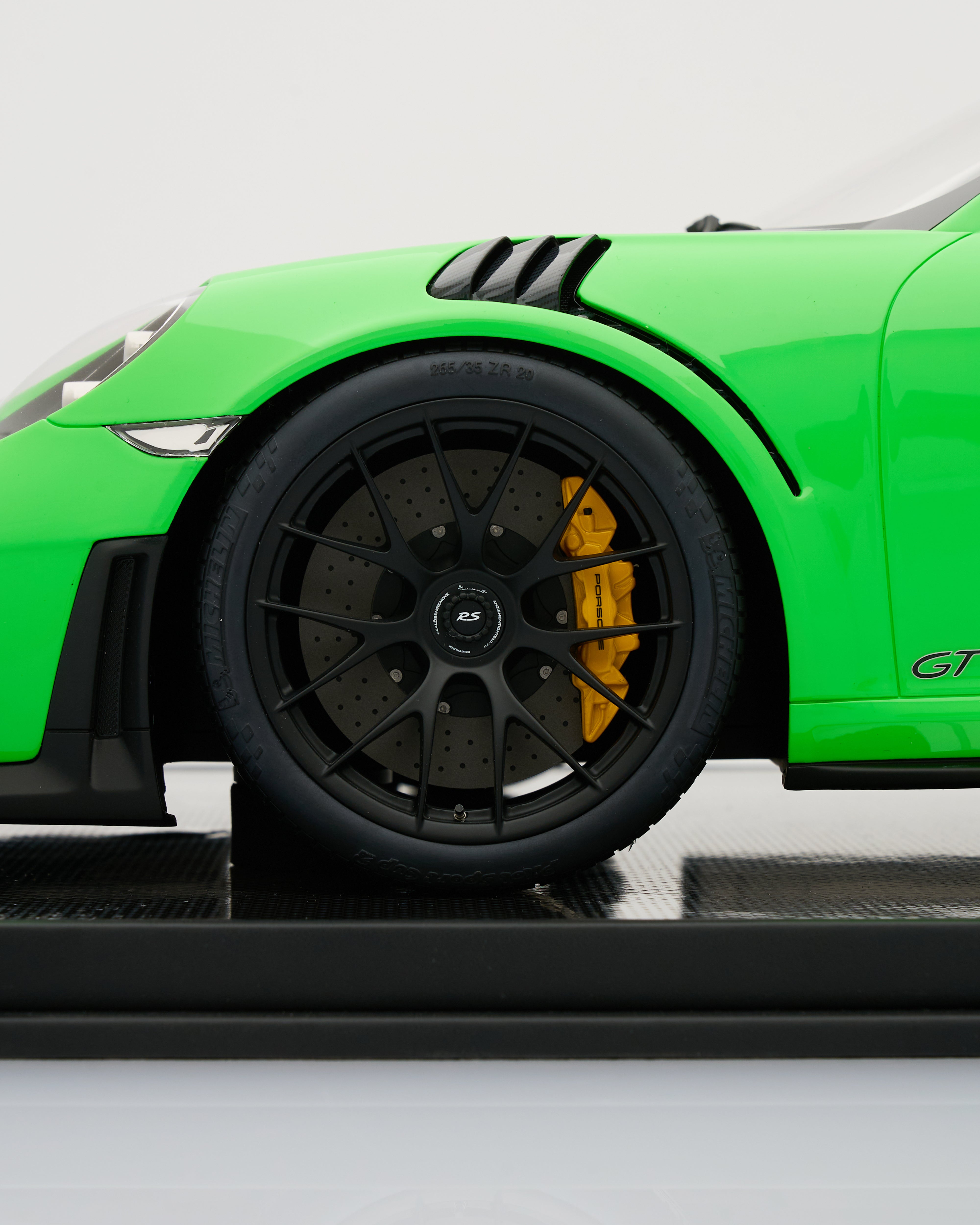 Close-up of a green sports car wheel with black rim and yellow brake caliper on a white background