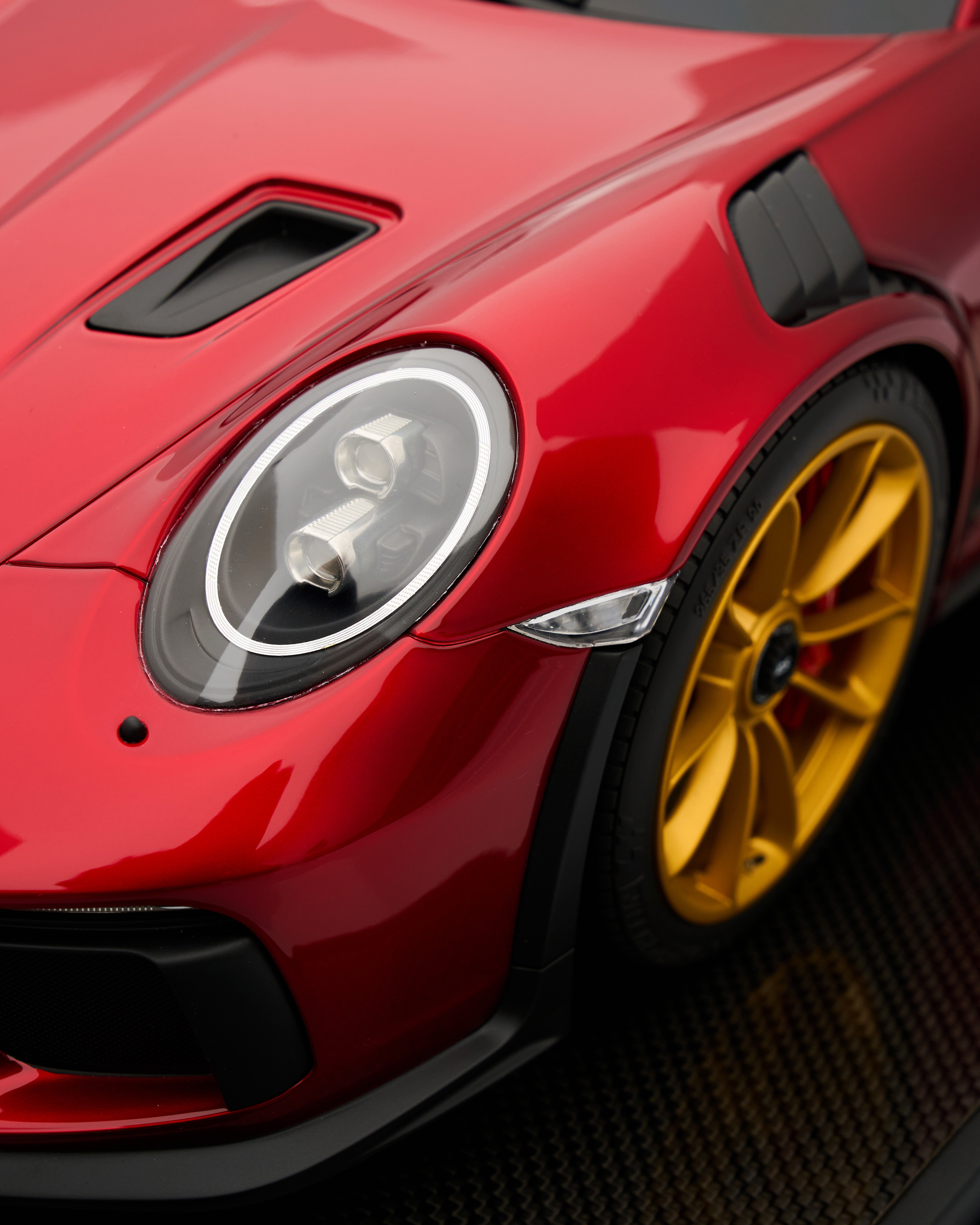 Close-up of a red sports car with yellow rims on a dark background
