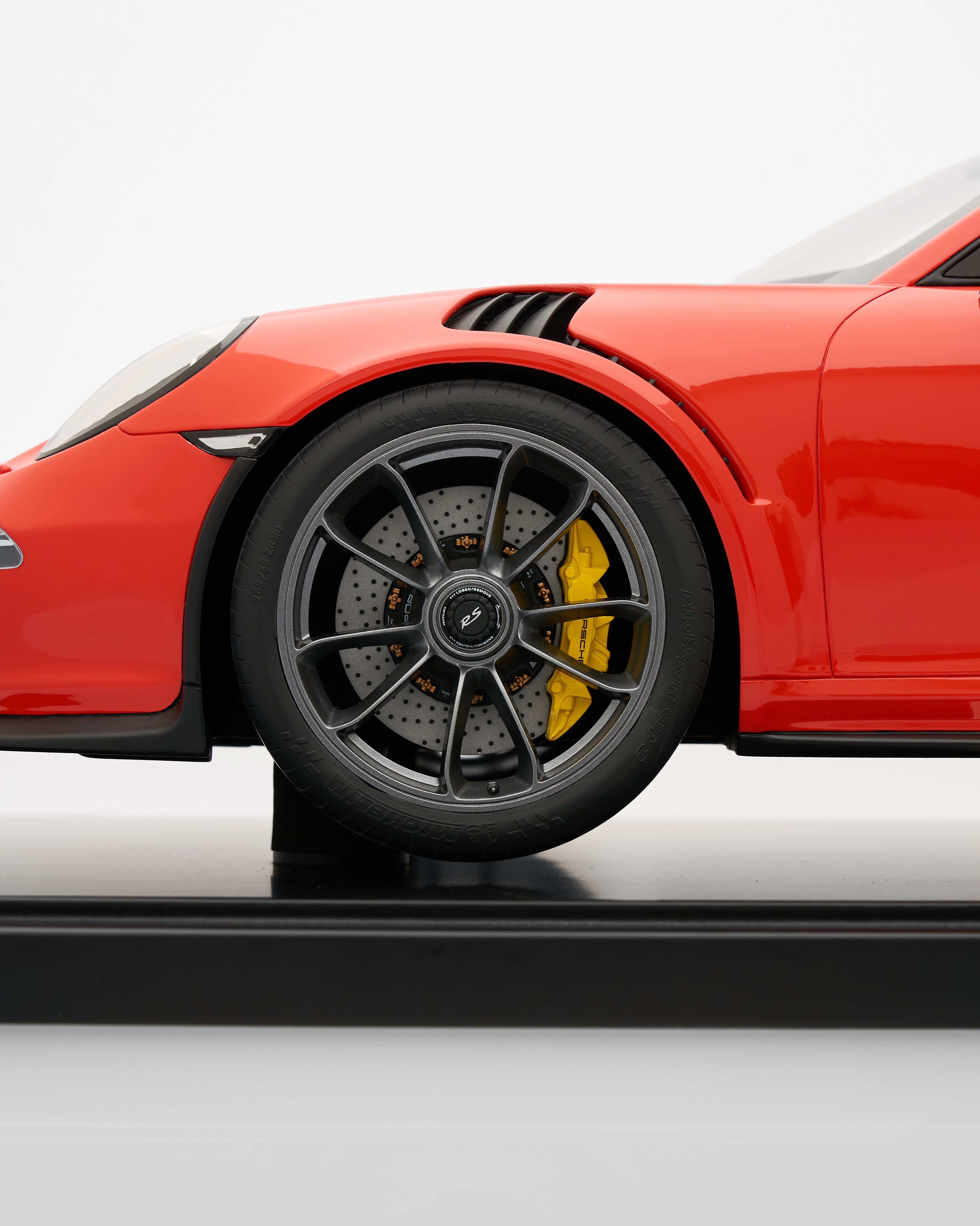 Close-up of a red sports car's wheel with black rim and yellow brake caliper on a white background