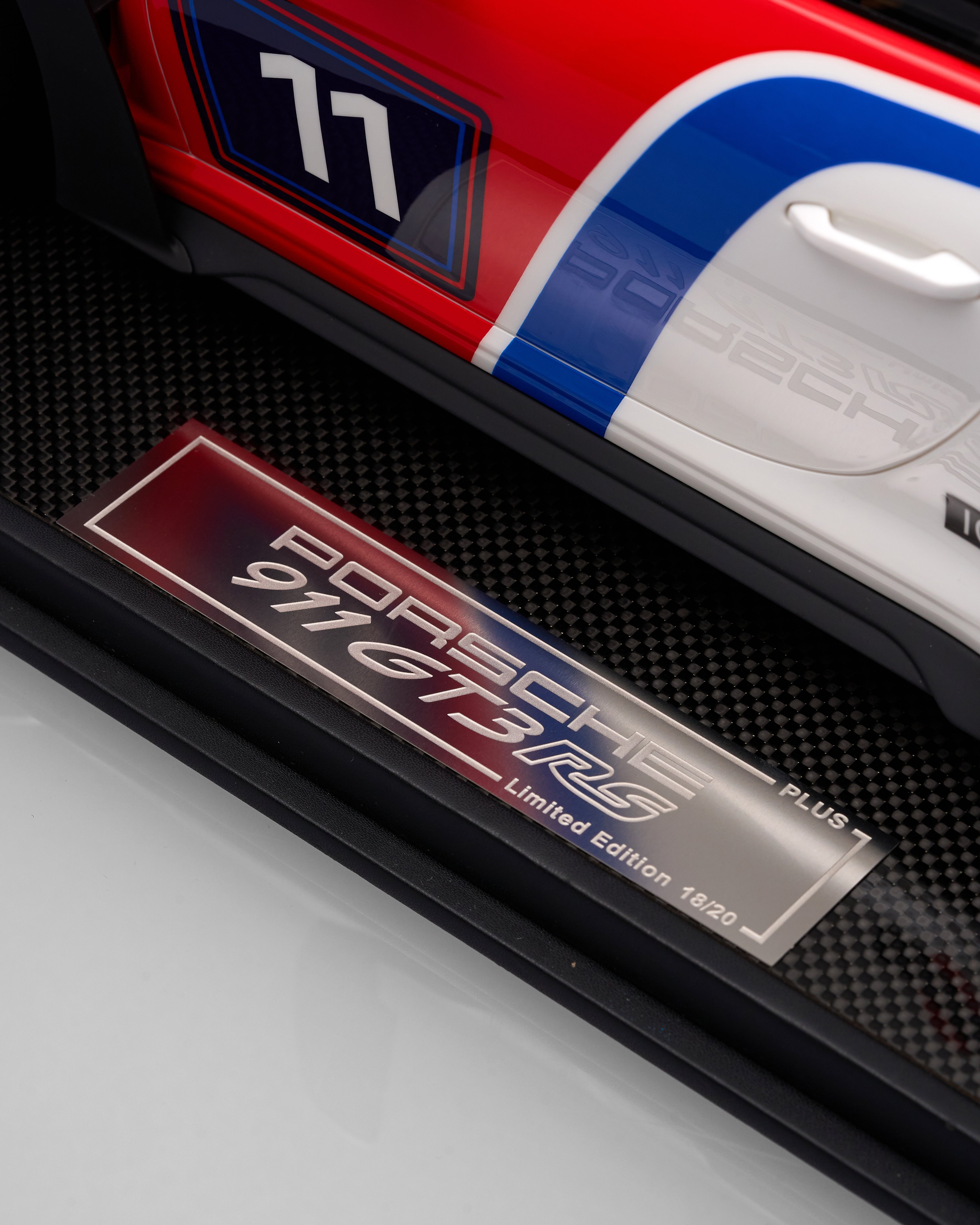 Close-up of a Porsche 911 car model with a limited edition plaque on a black carbon fiber background.