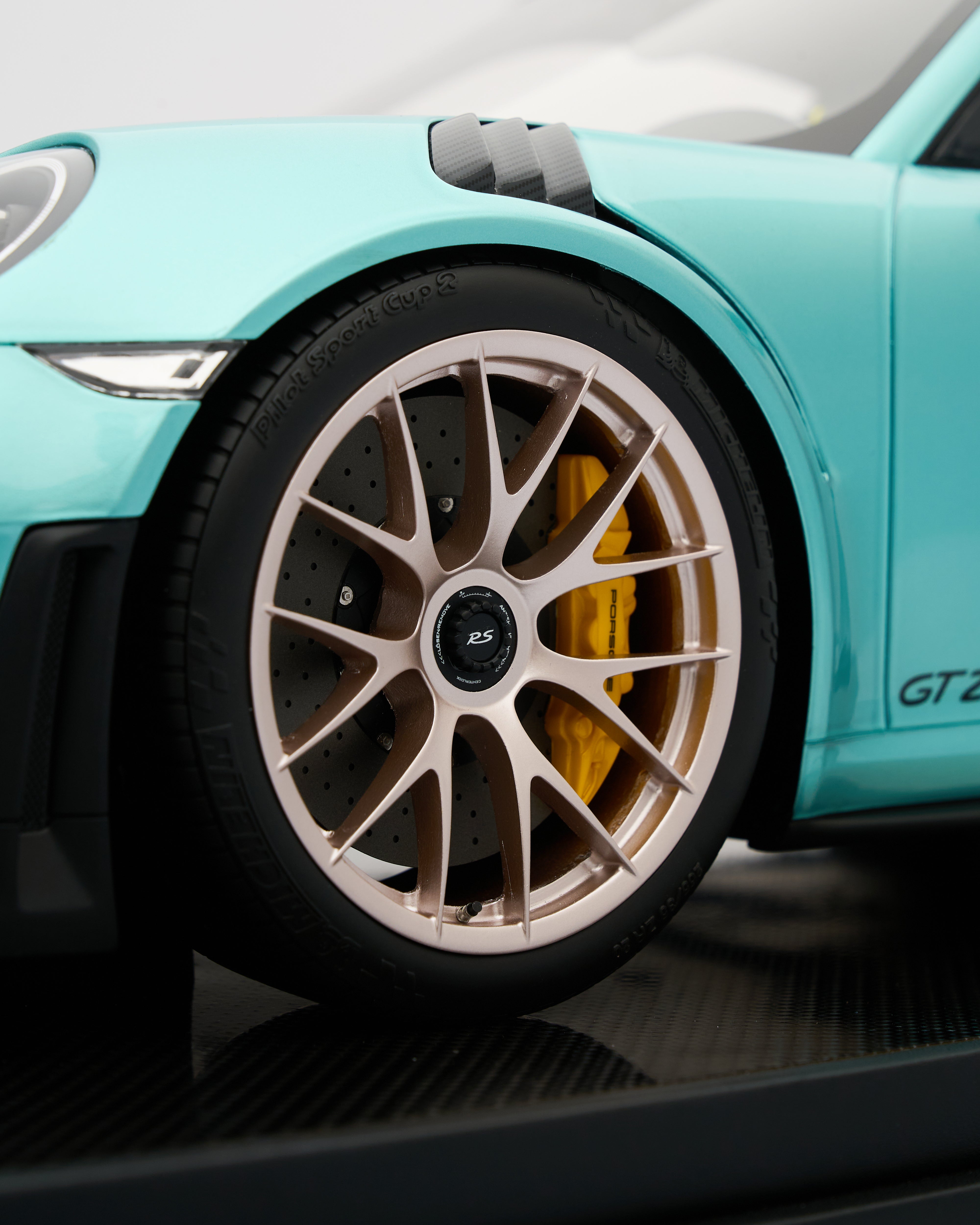 Close-up of a turquoise car wheel with a gold brake caliper on a reflective surface.