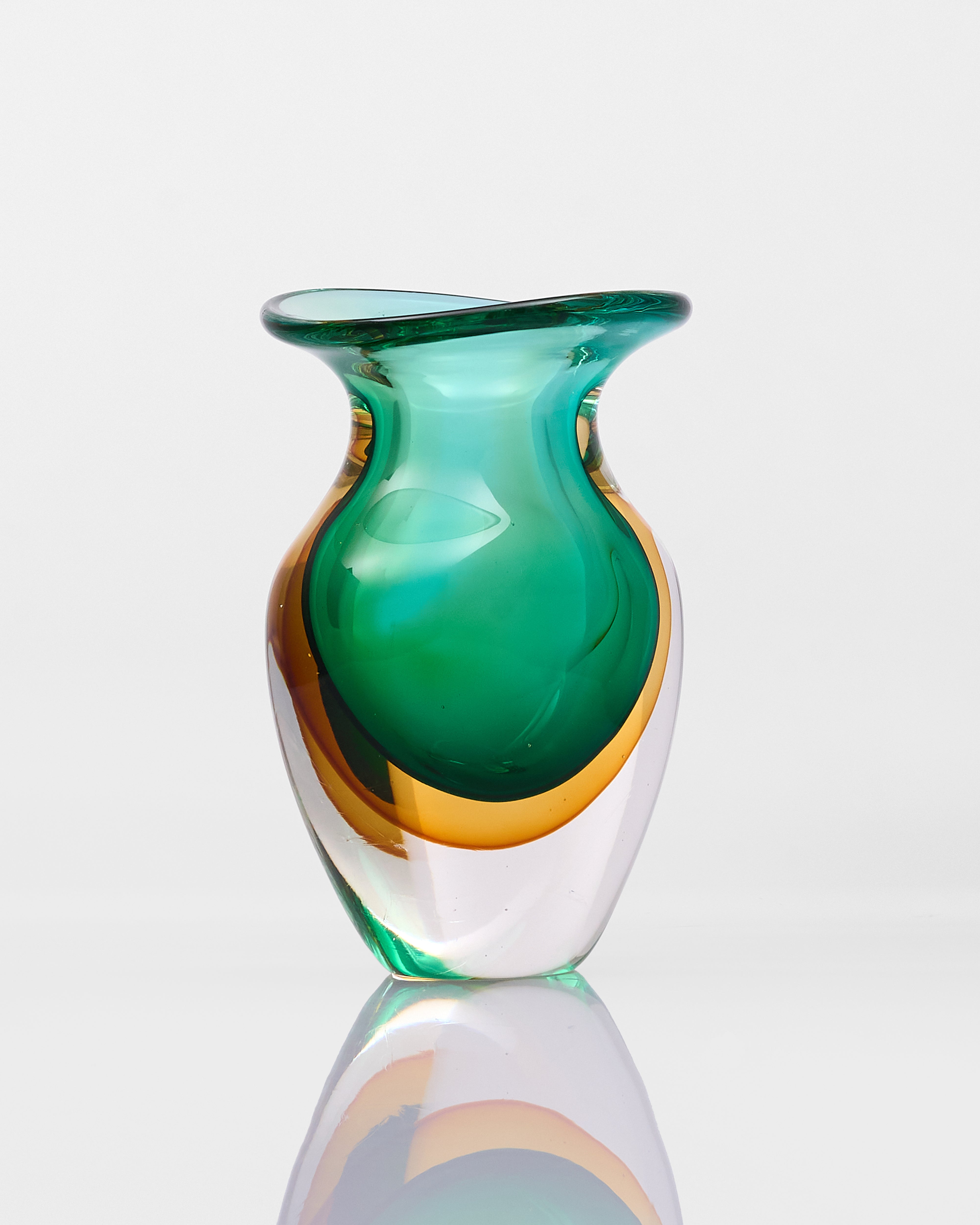 Green and gold glass vase on a reflective surface with a white background