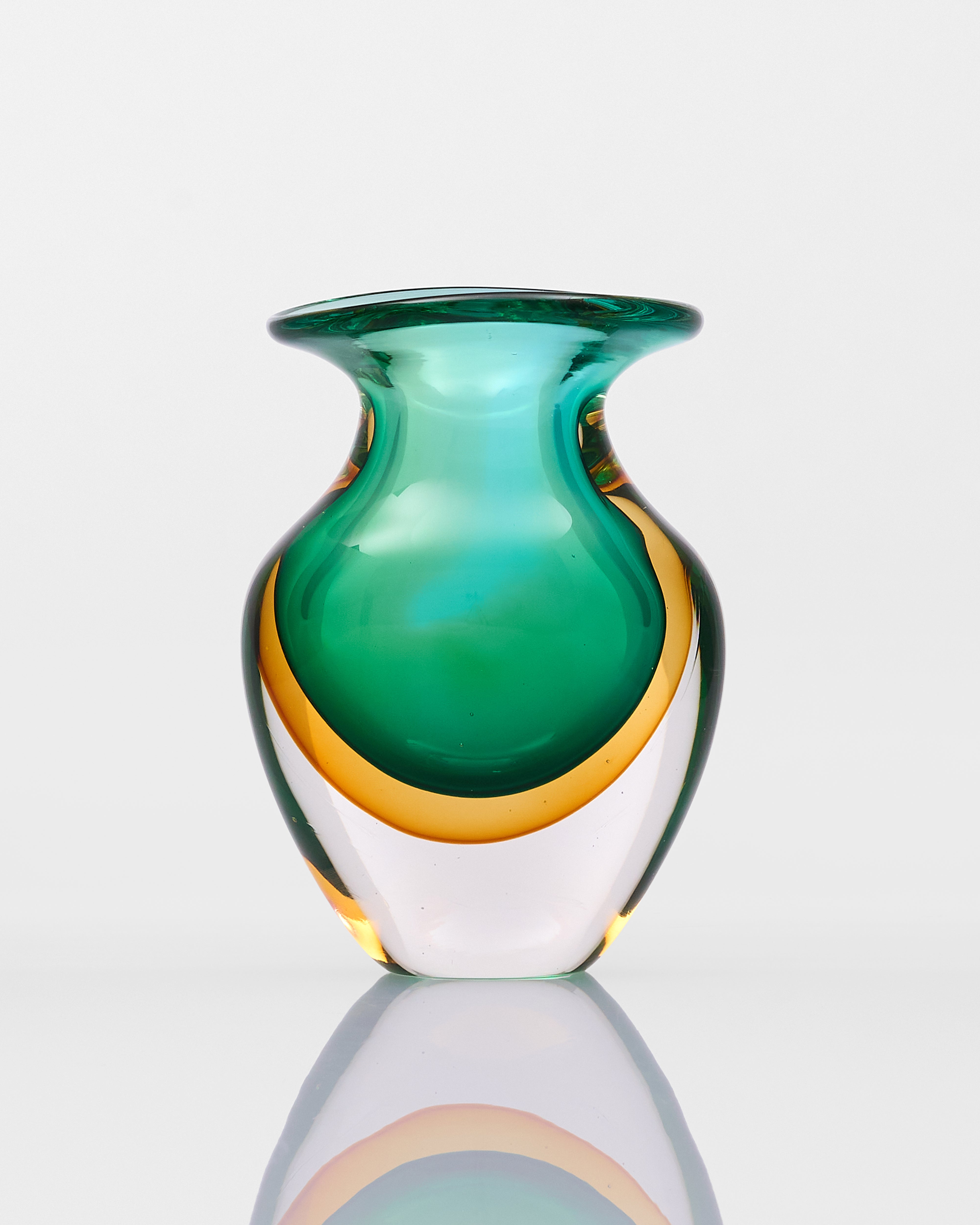Green and gold glass vase on a reflective surface with a white background