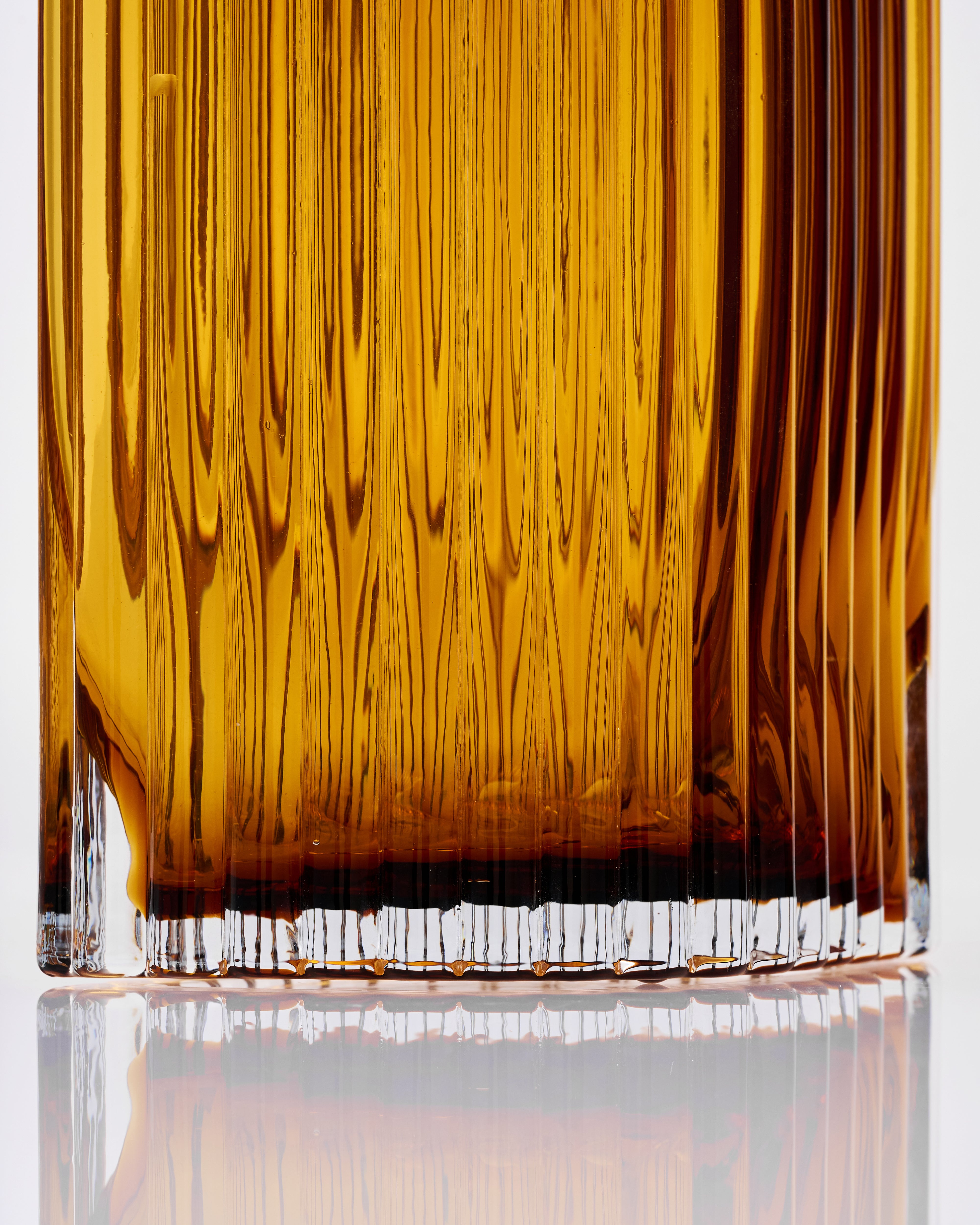 Close-up of a glass with amber vase ribbed on a reflective surface