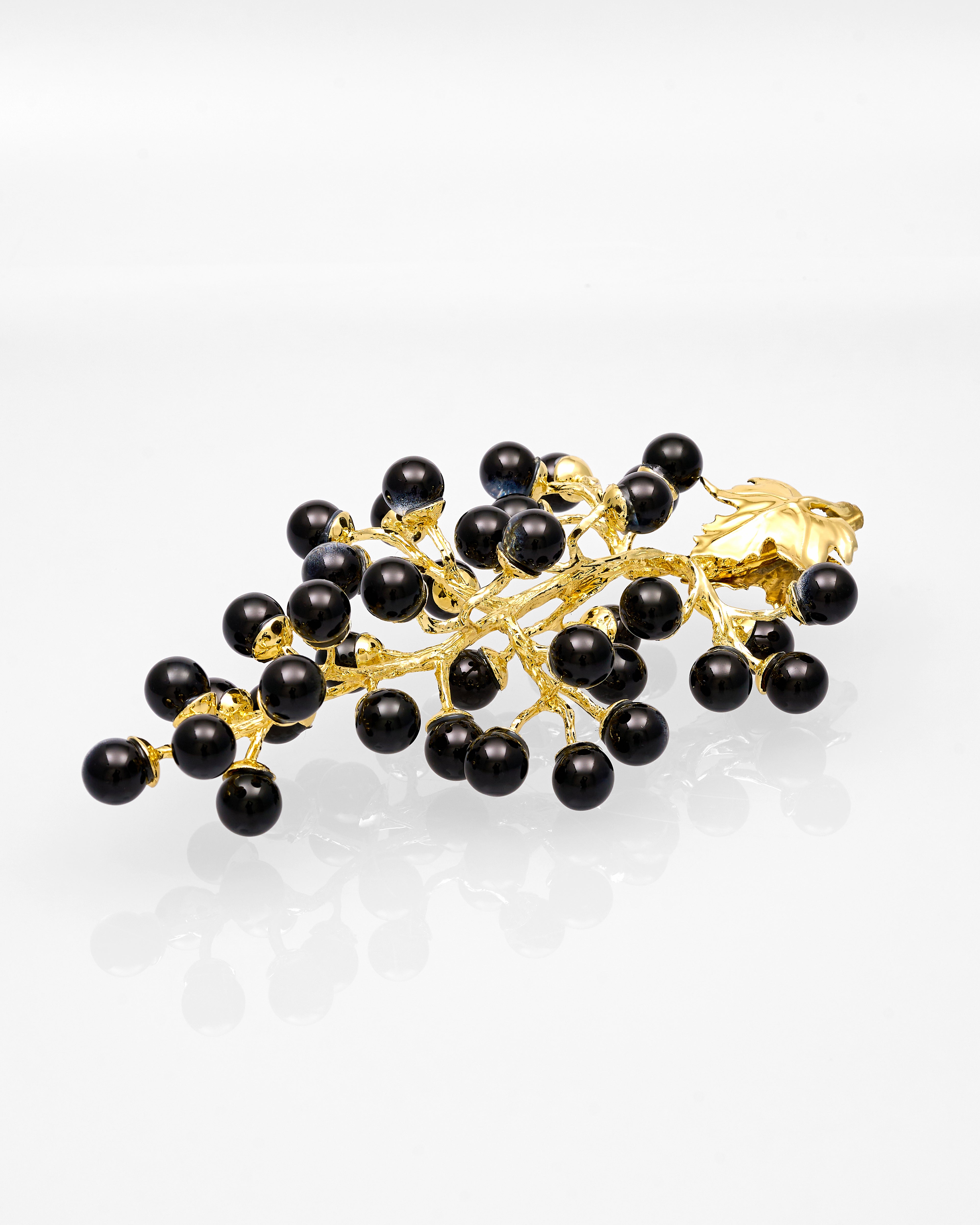 Gold branch-shaped grape decor with black beads on a white background