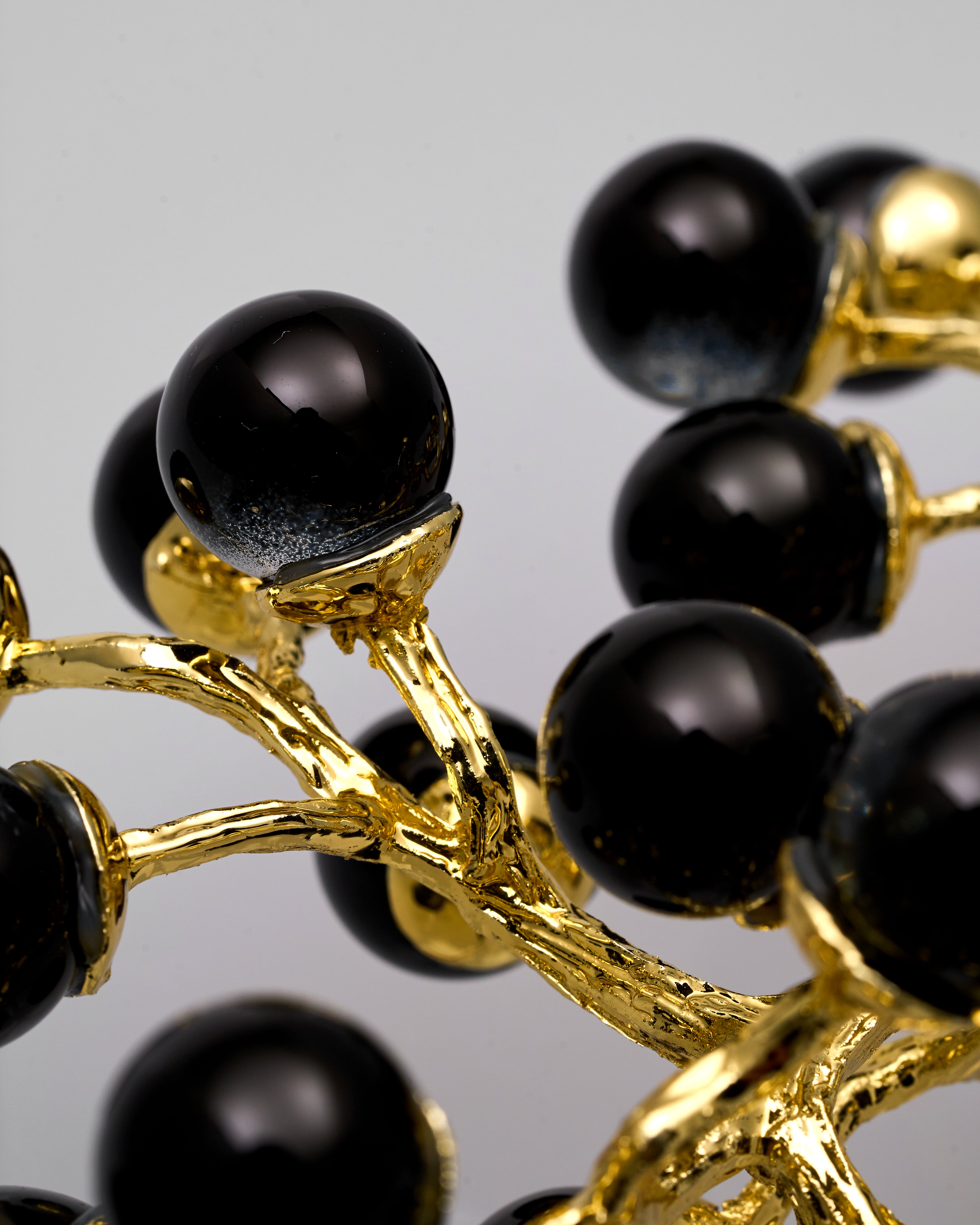 Close-up of a grape metal decor with black beads and gold branches on a gray background