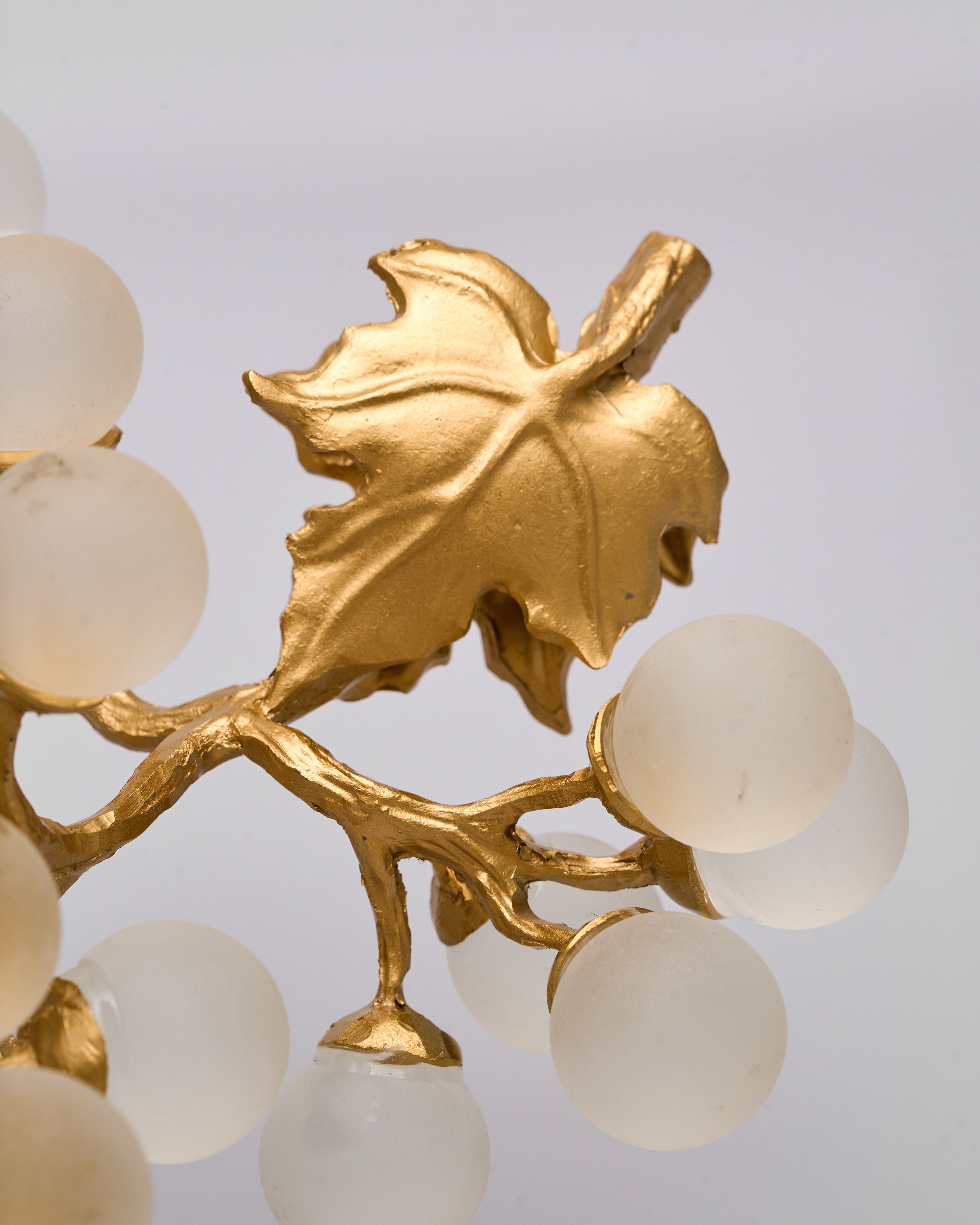 Decorative gold fixture with leaf design and white spherical elements on a light gray background