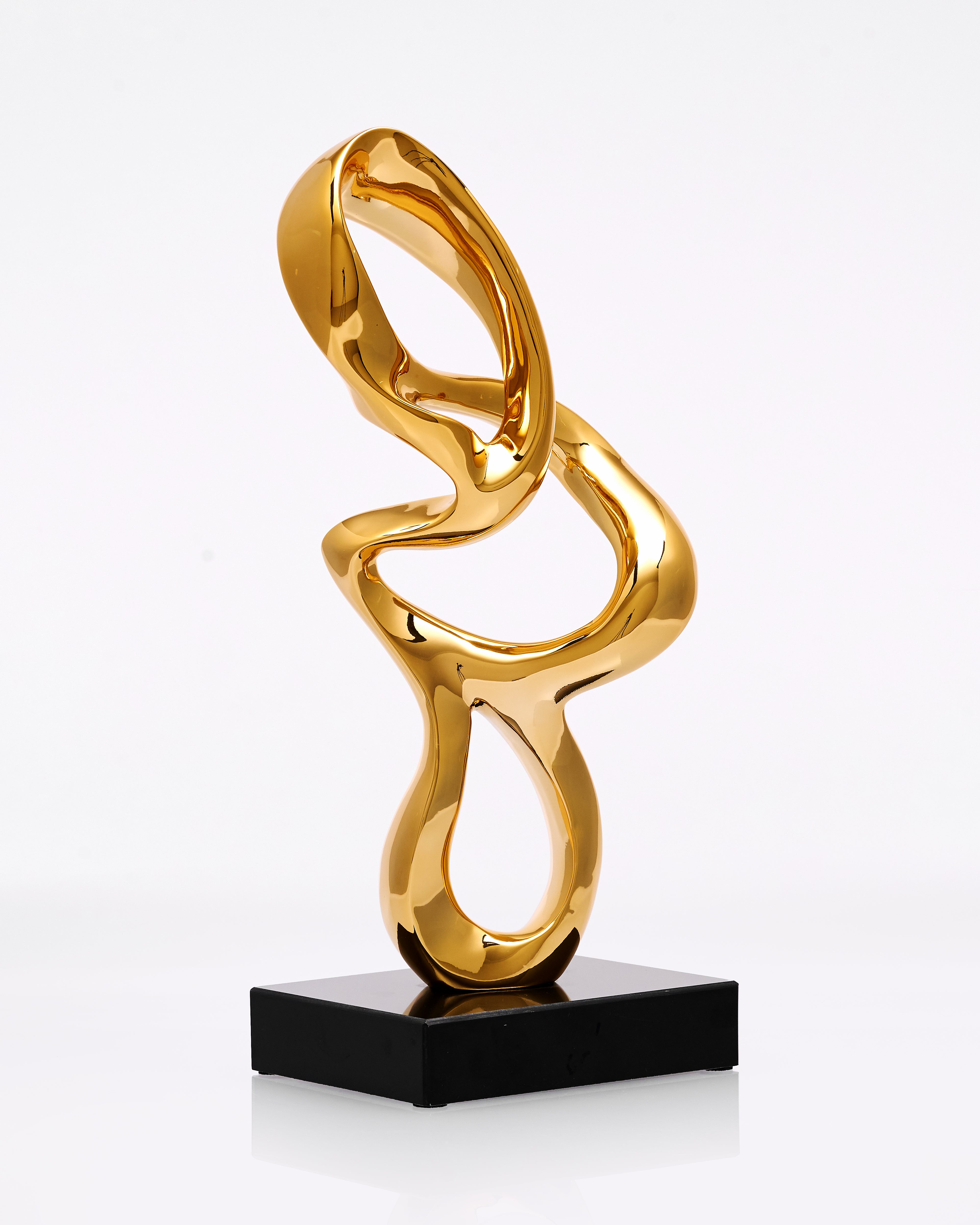 Gold abstract sculpture on a black base against a white background