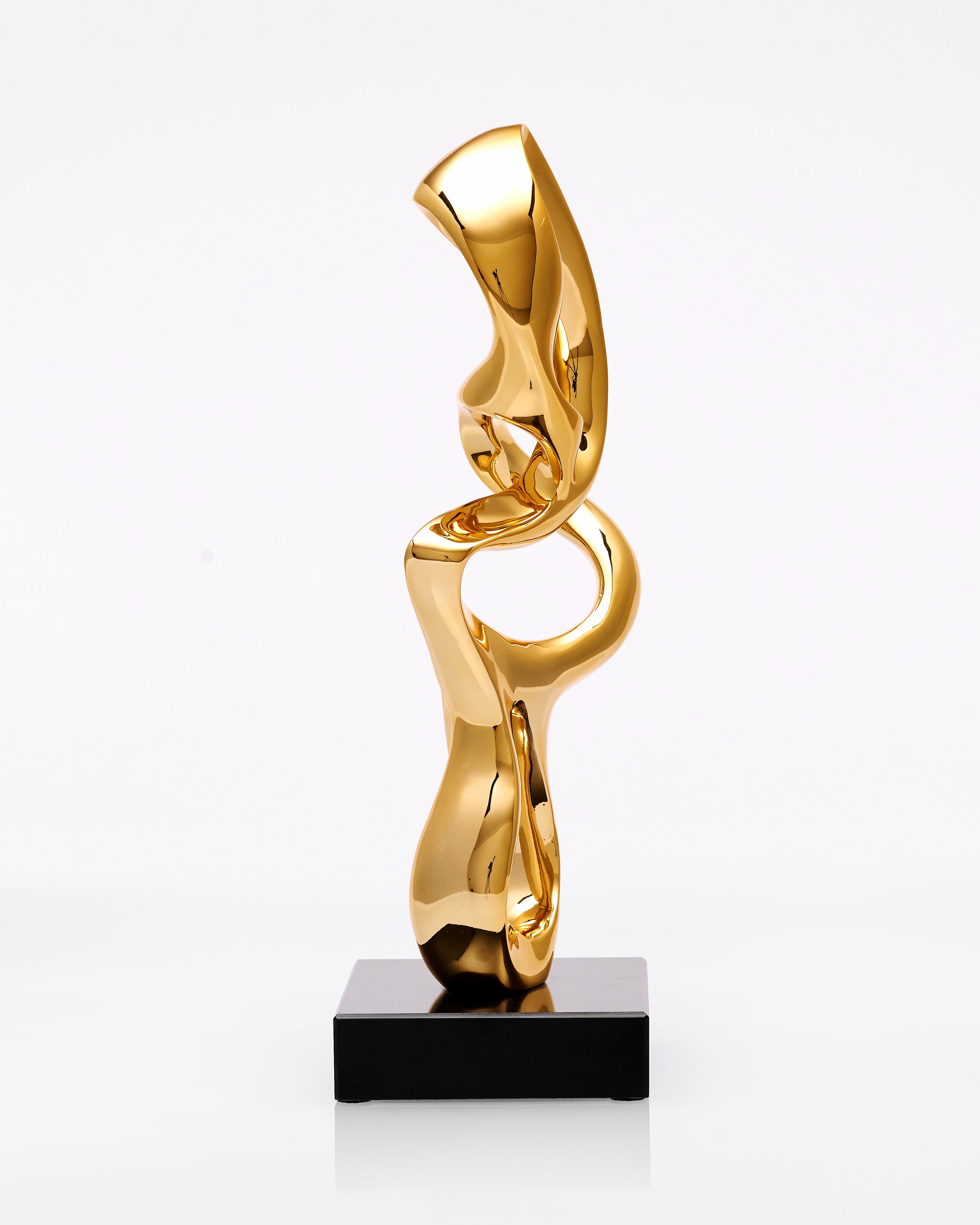 Gold abstract sculpture on a black base against a white background