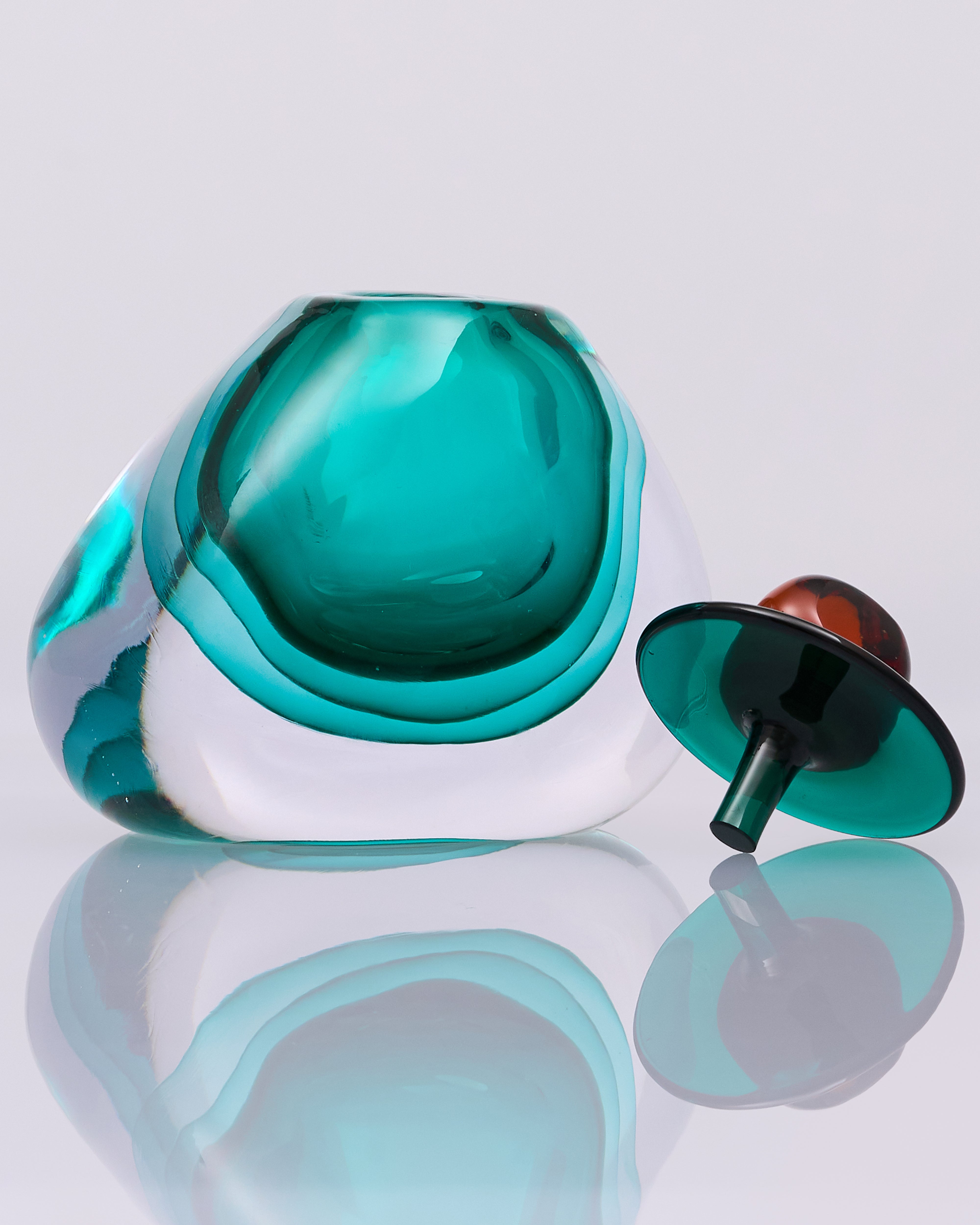 Teal and white glass object on a reflective surface with a white background