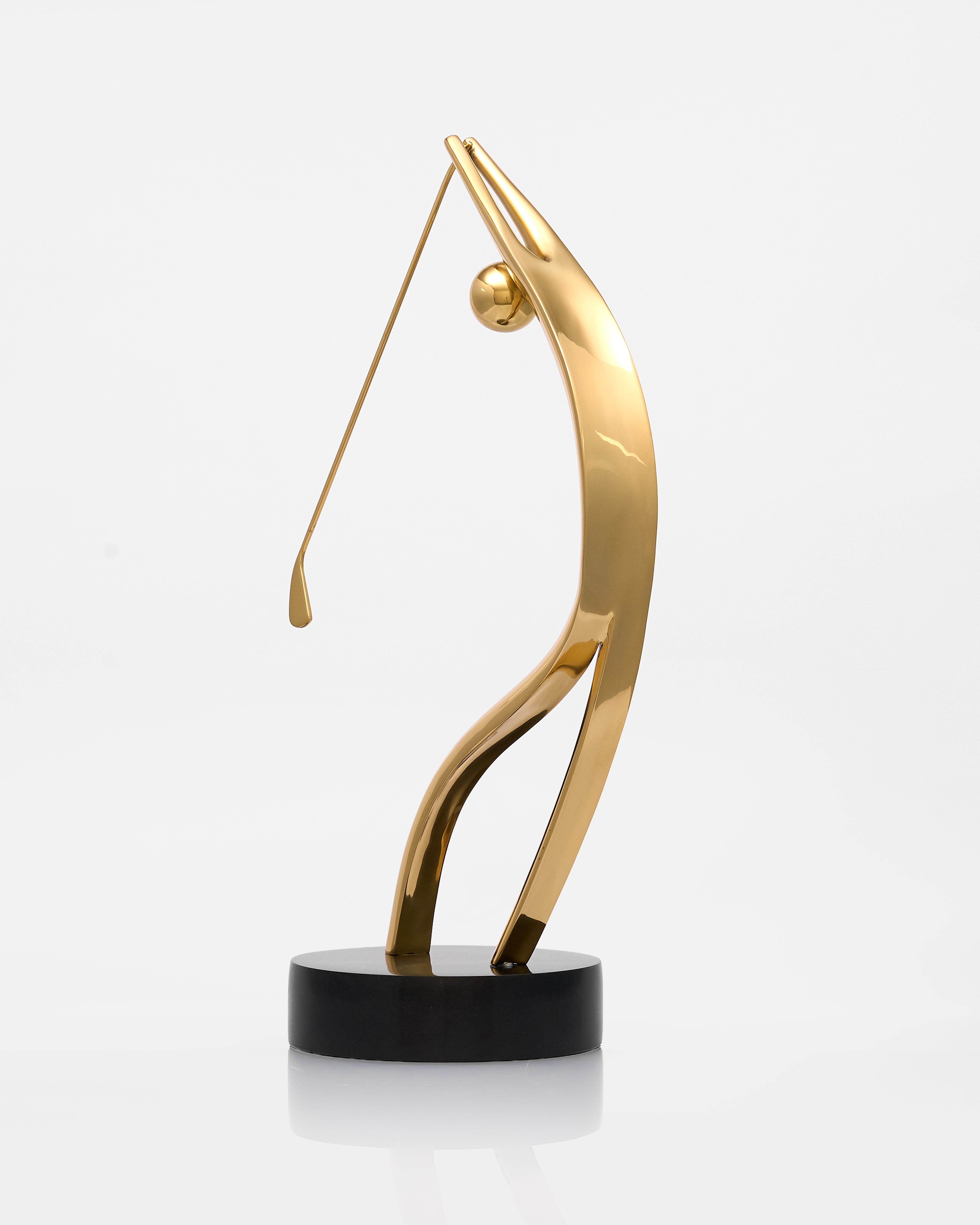 Gold abstract sculpture on a black base against a white background