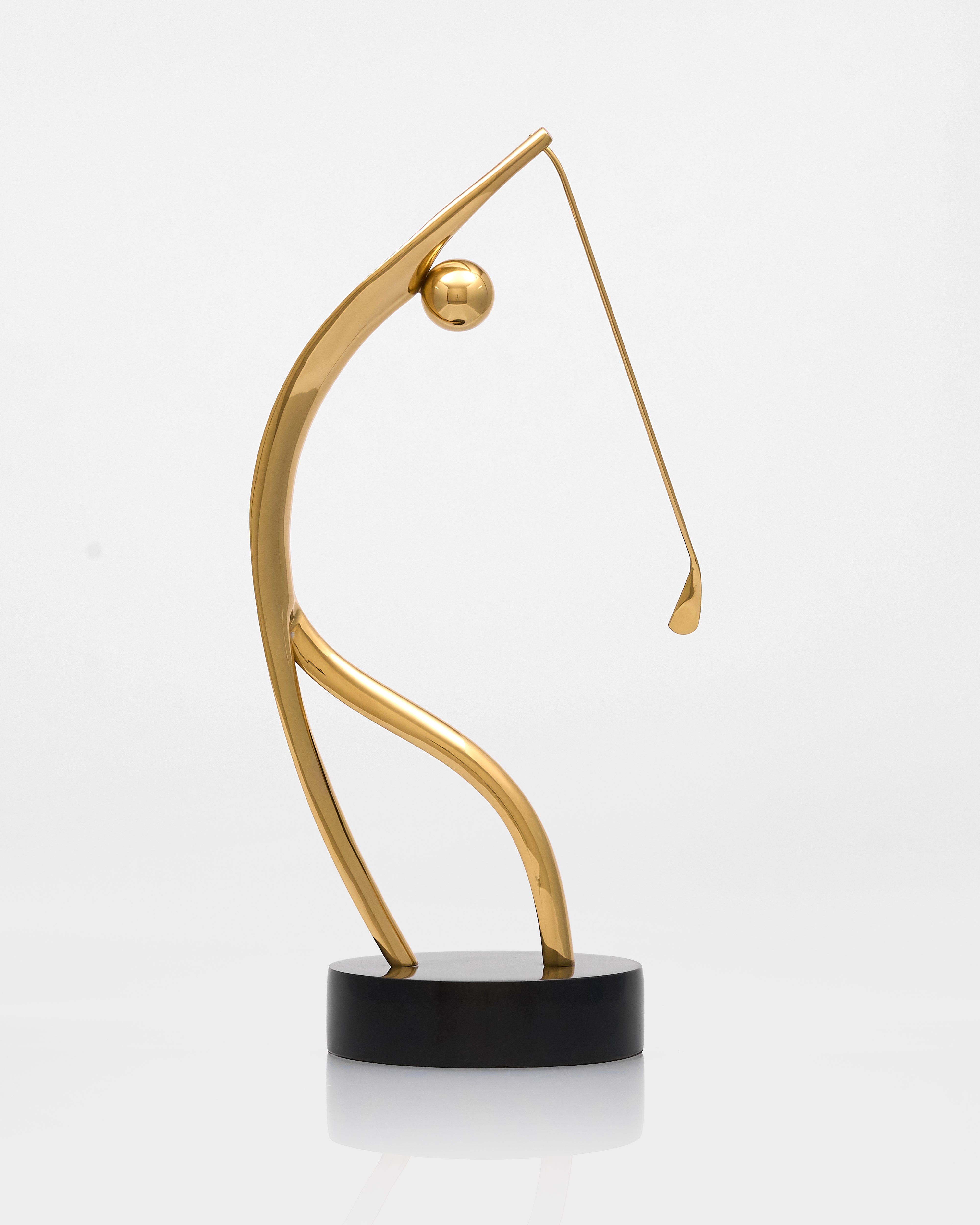 Gold abstract sculpture on a black base against a white background