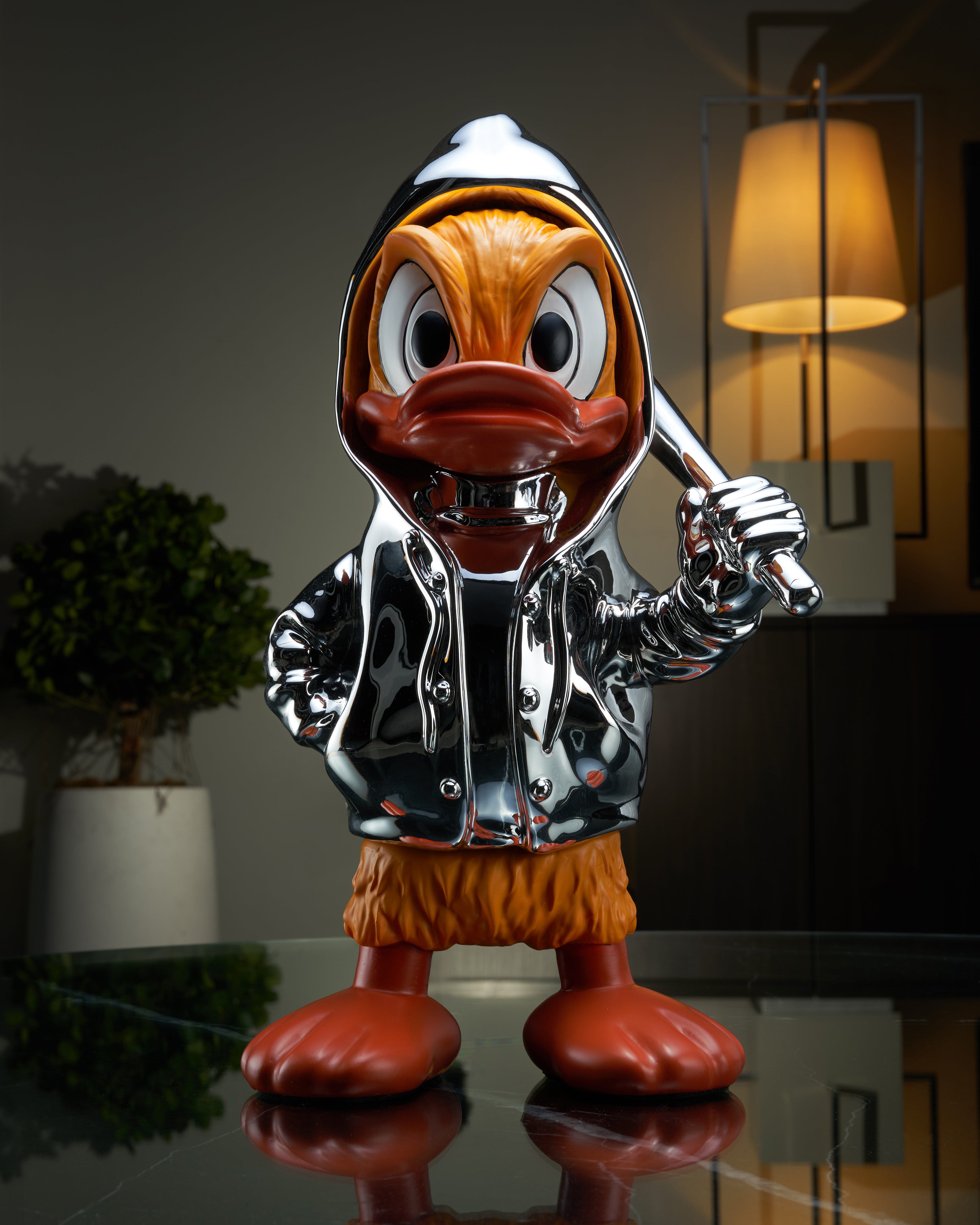 Metallic Donald Duck figurine holding a bat on a reflective surface with a blurred background.