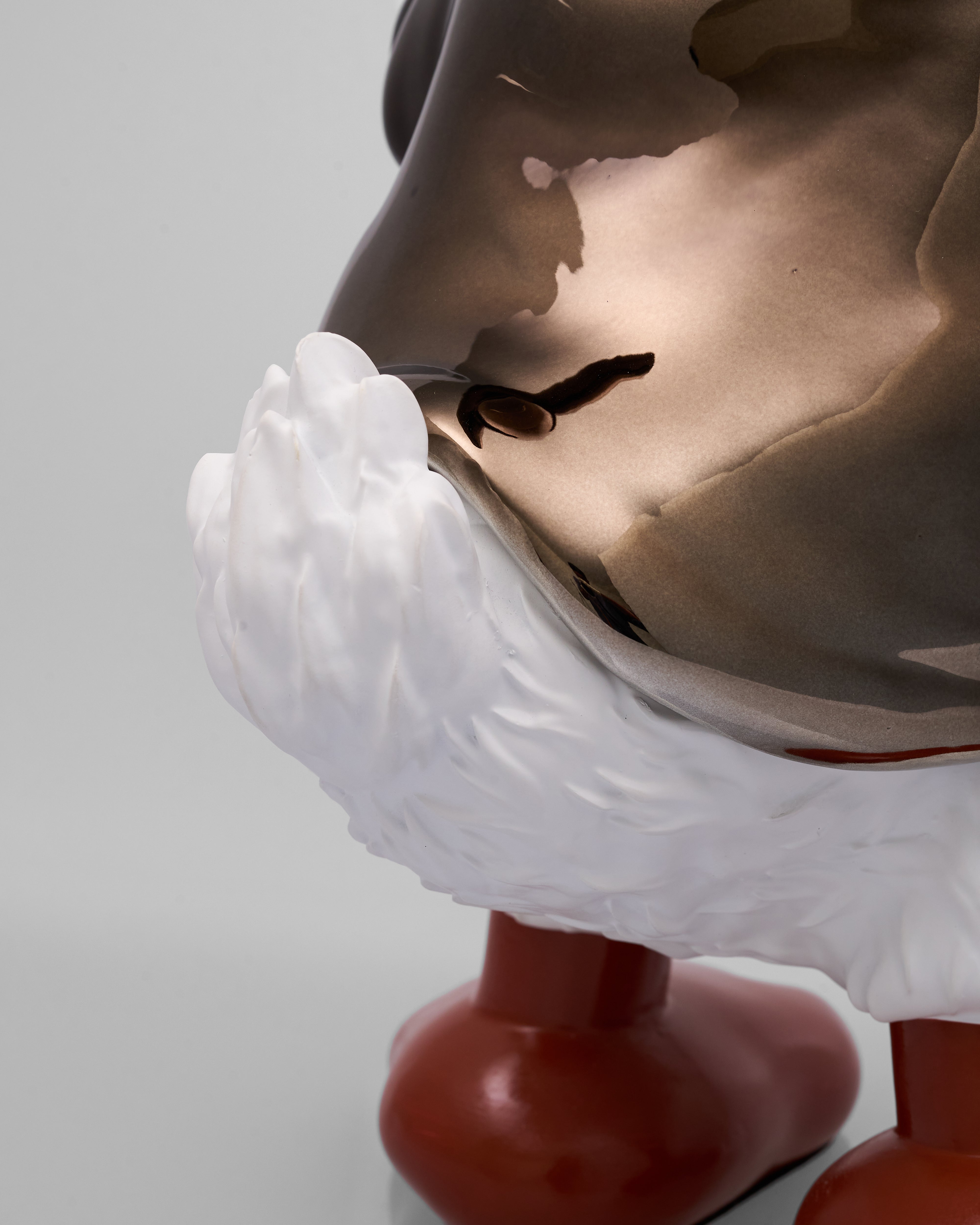 Close-up of a sculpture with a detailed face and white feathers on a gray background
