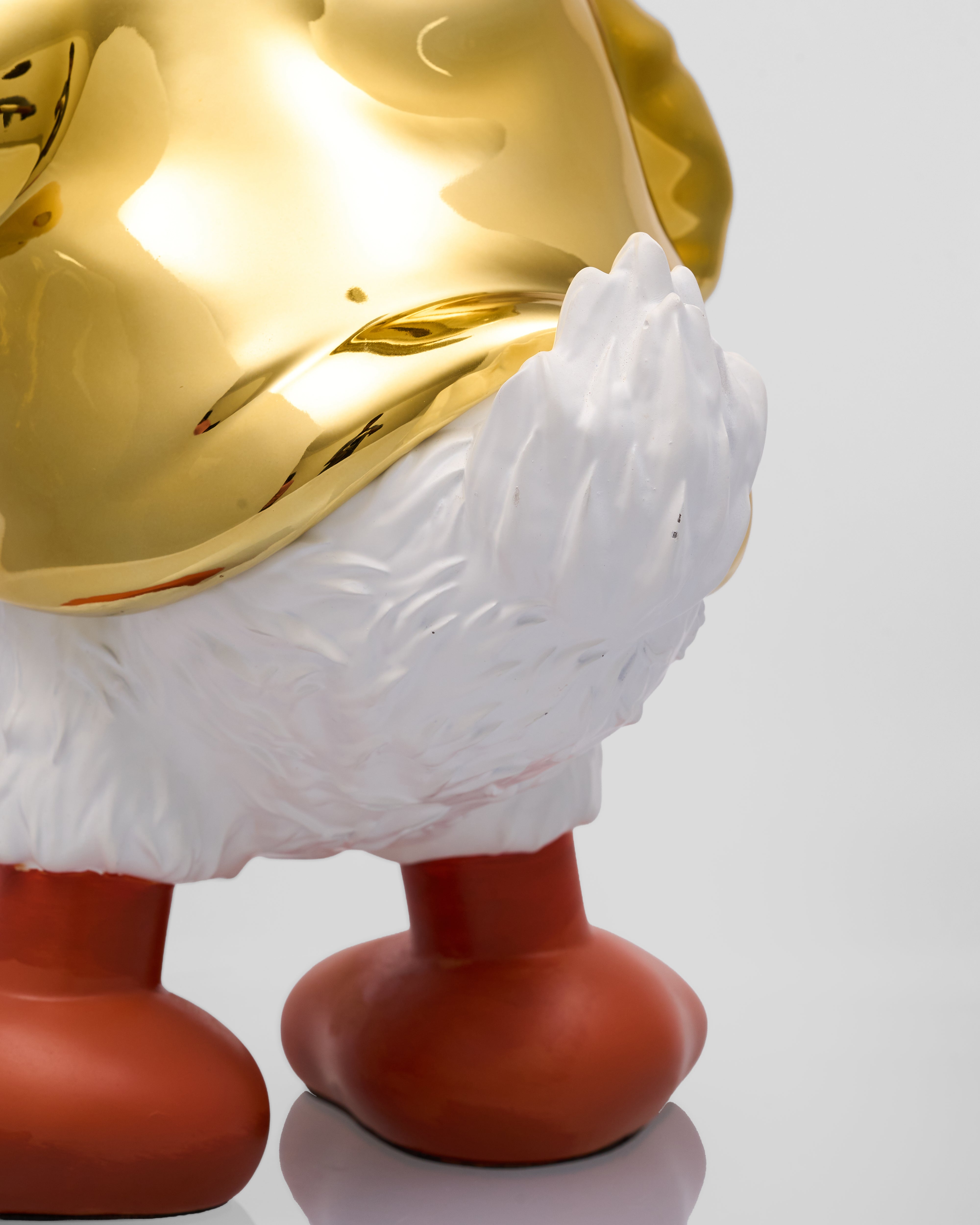 Decorative object with gold head, white feathers, and red base on a light gray background