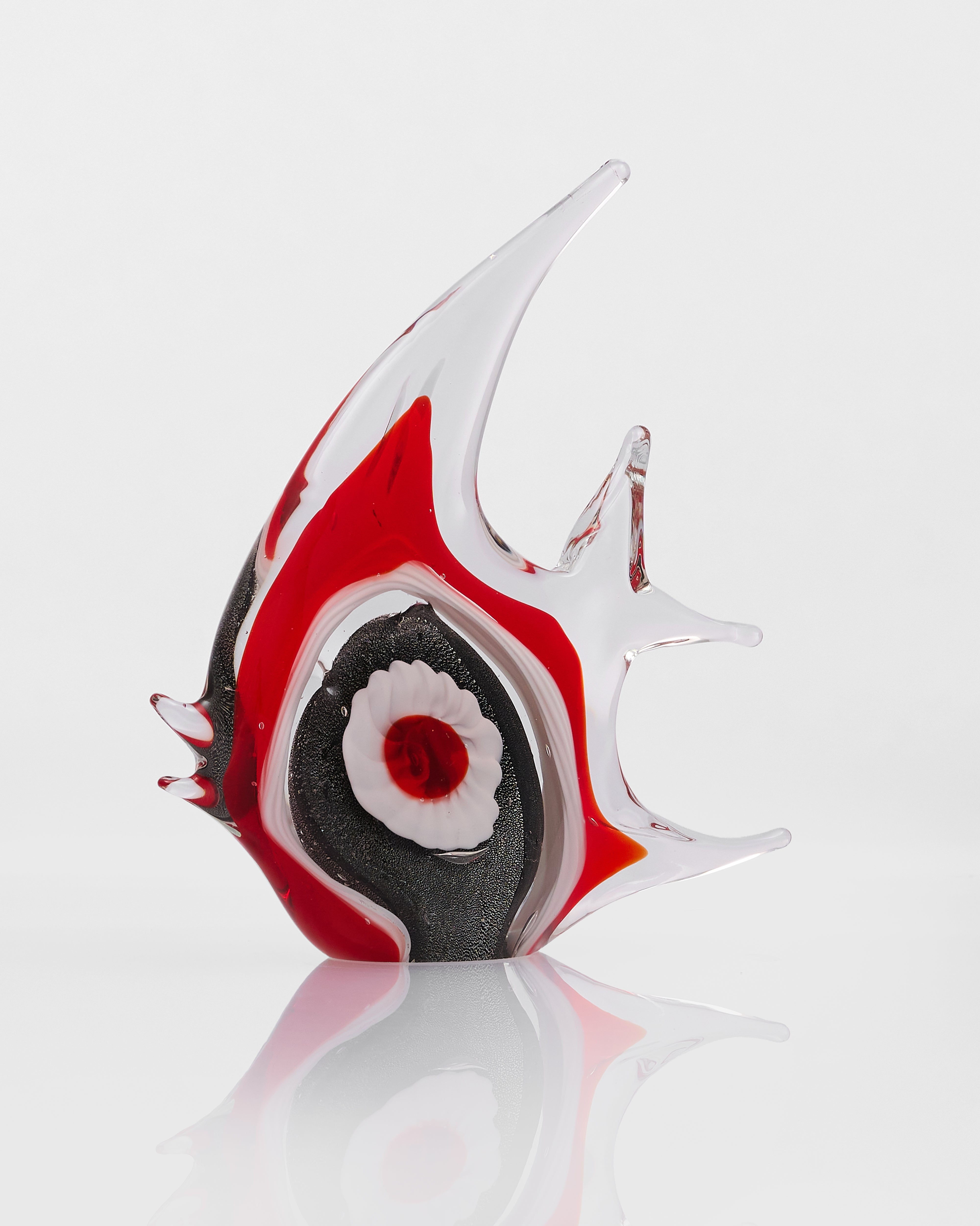 Glass sculpture of a fish with red, black, and white colors on a reflective surface.