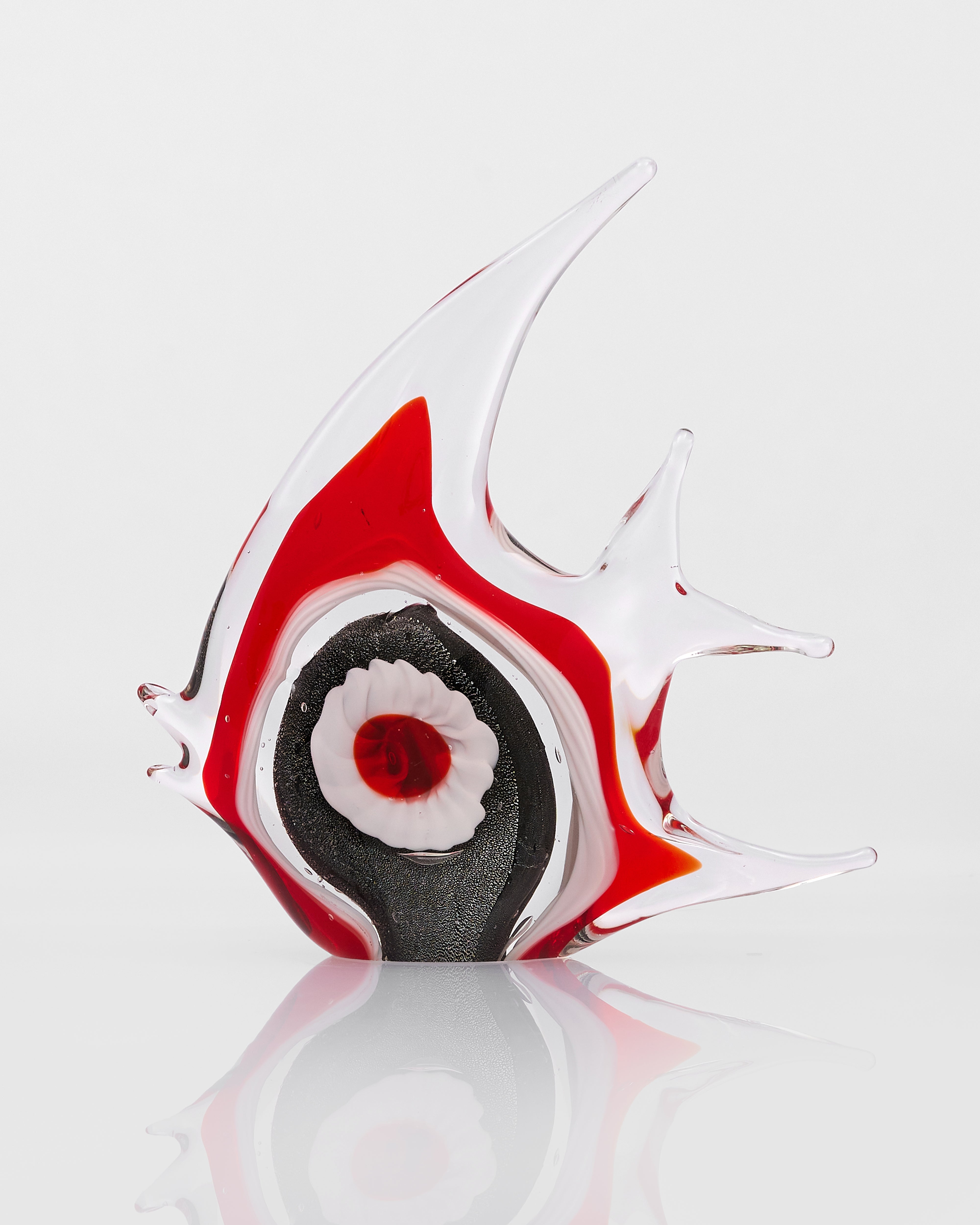 Glass sculpture of a fish with red, black, and white colors on a reflective surface.