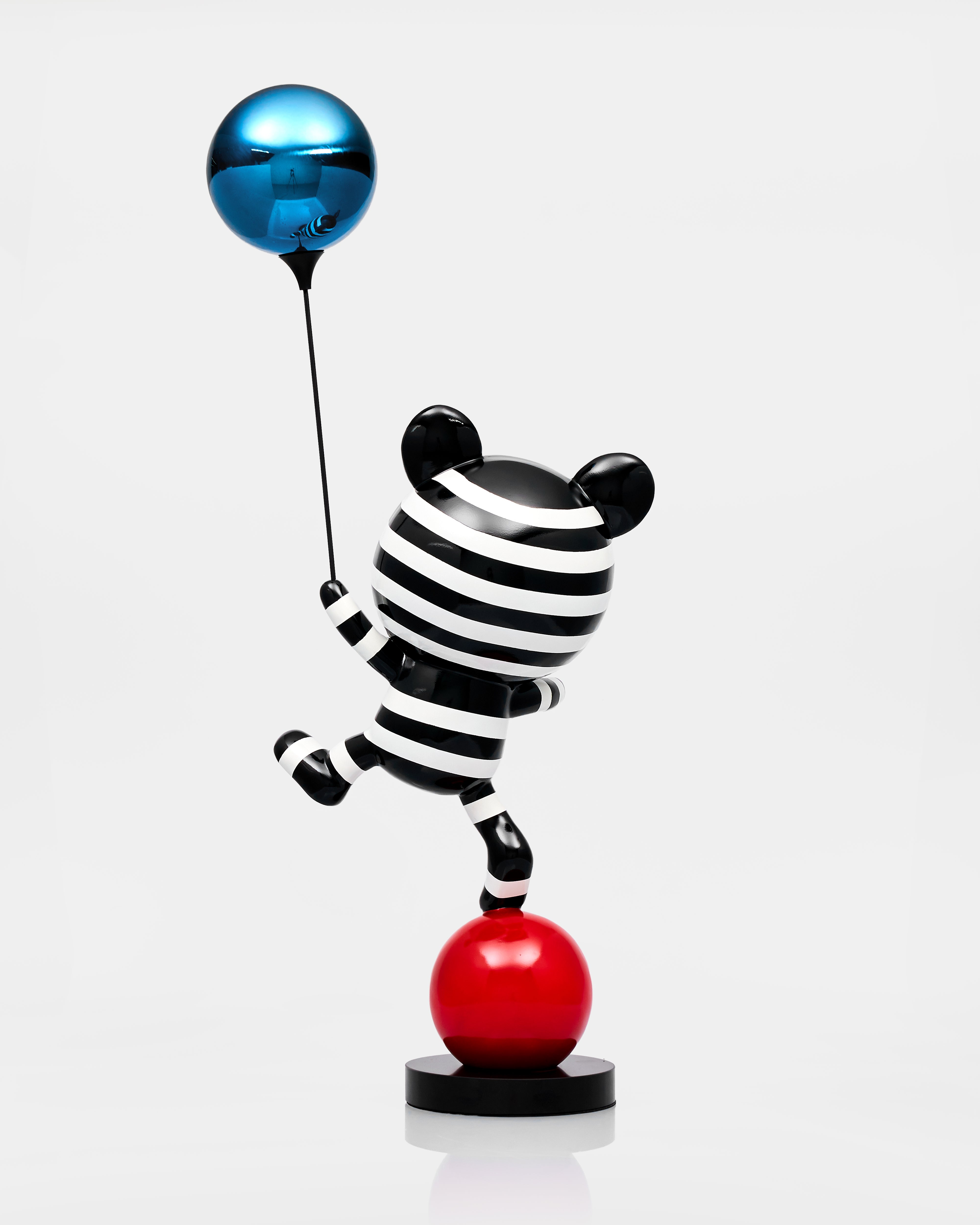 Black and white striped cat figurine with a blue balloon and red ball on a white background