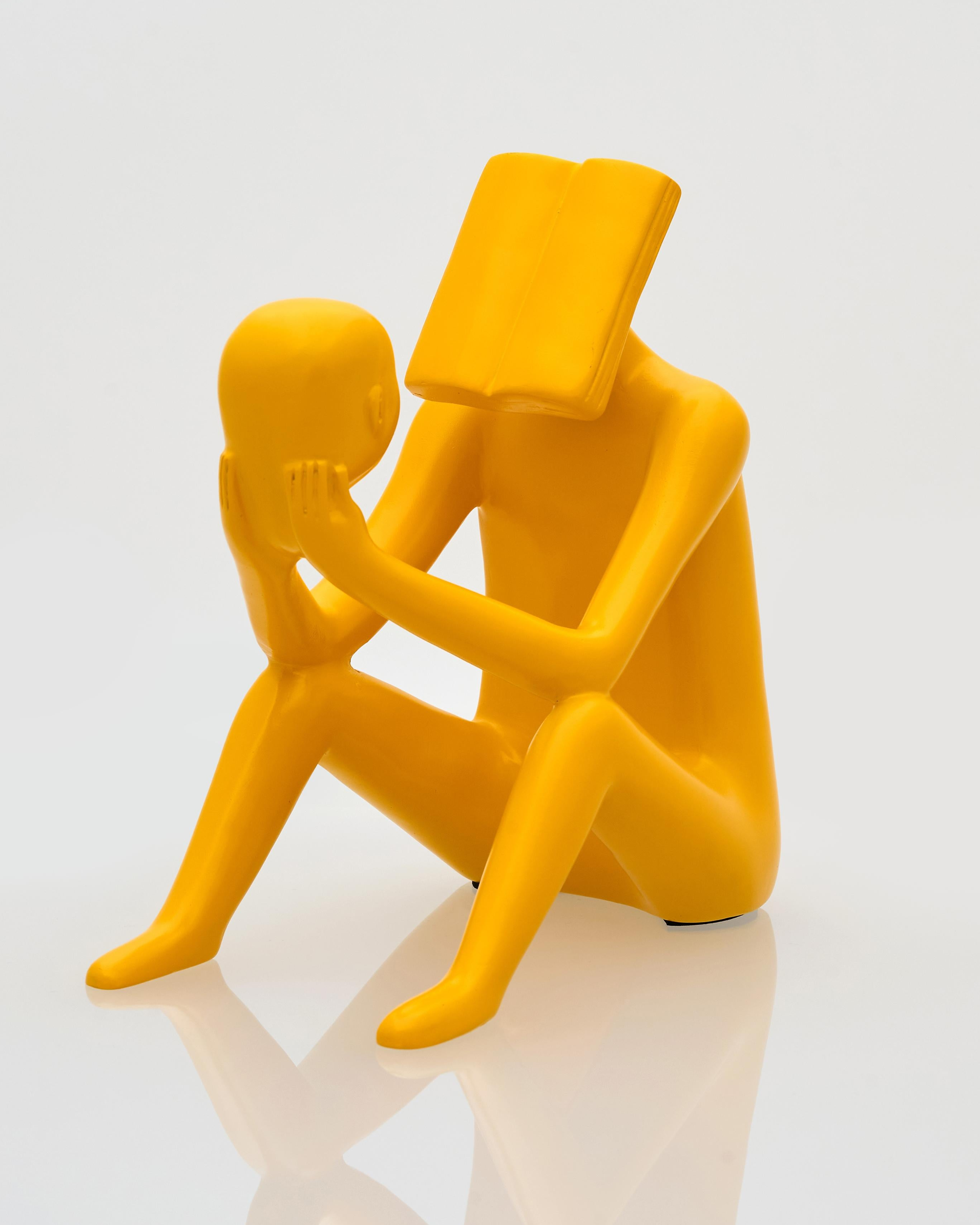Yellow sculpture of two abstract figures on a white background reading book