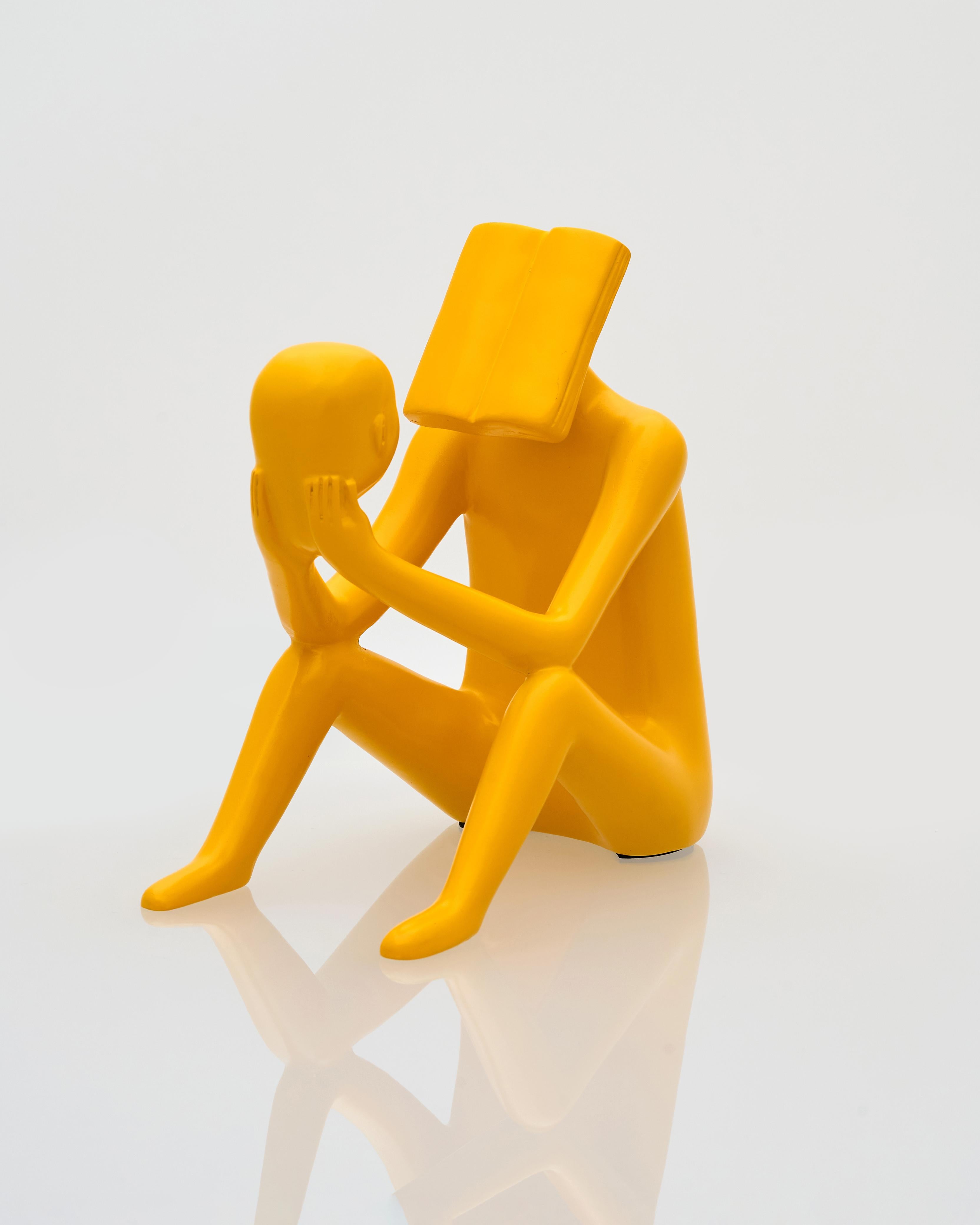 Yellow sculpture of two abstract figures embracing on a white background