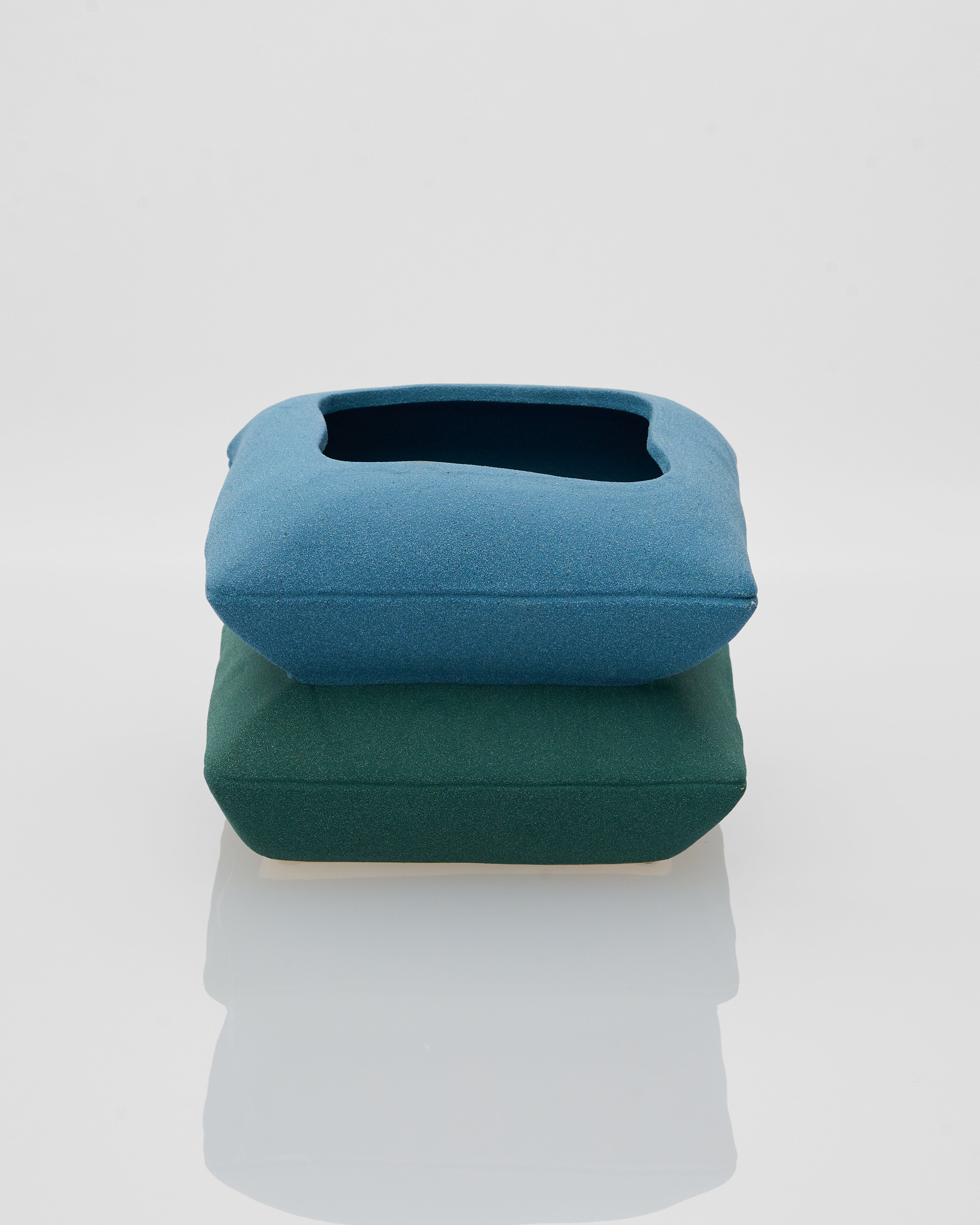 Two blue and green cushions stacked on a white background