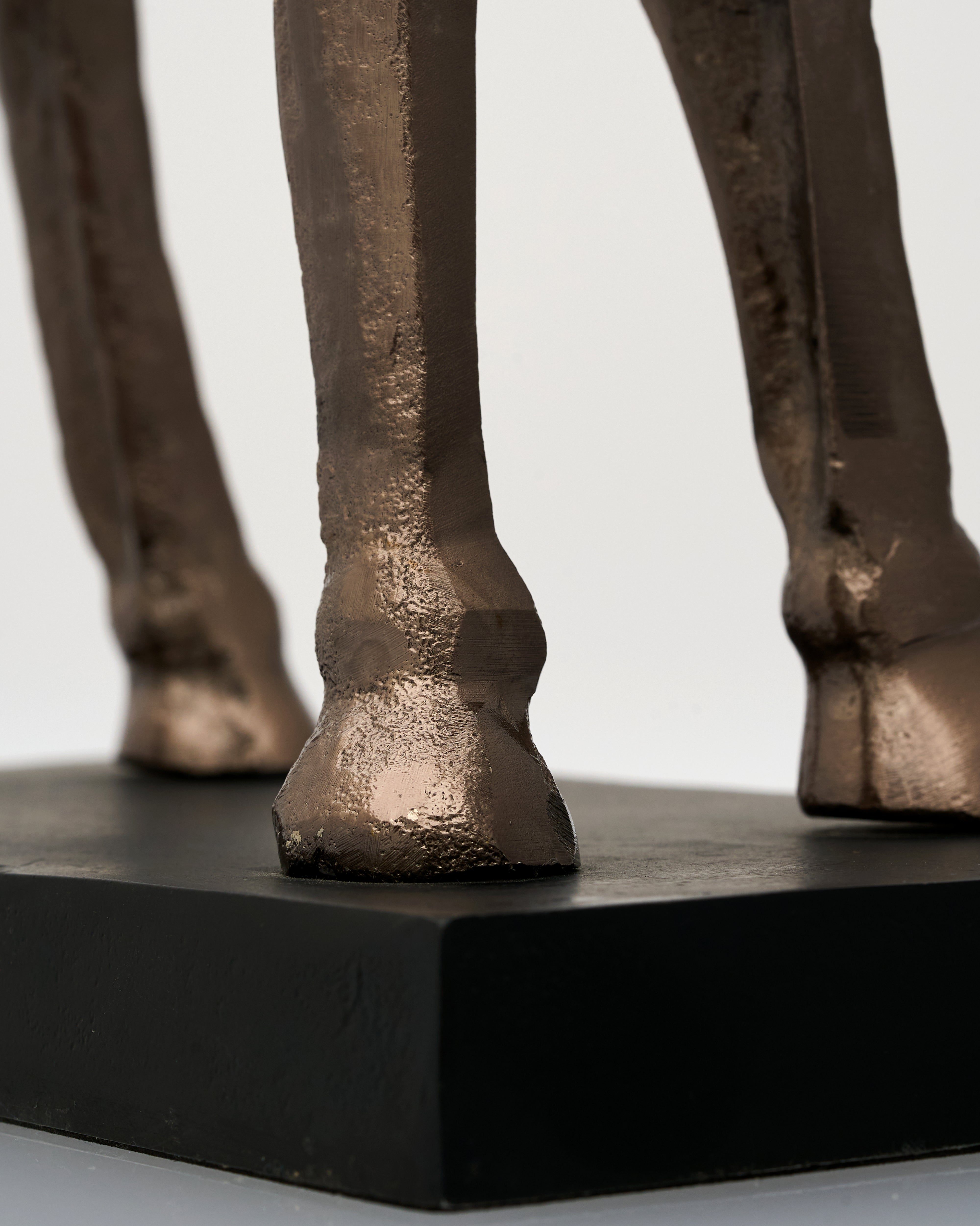 Bronze sculpture of a camel's legs on a black base against a light background