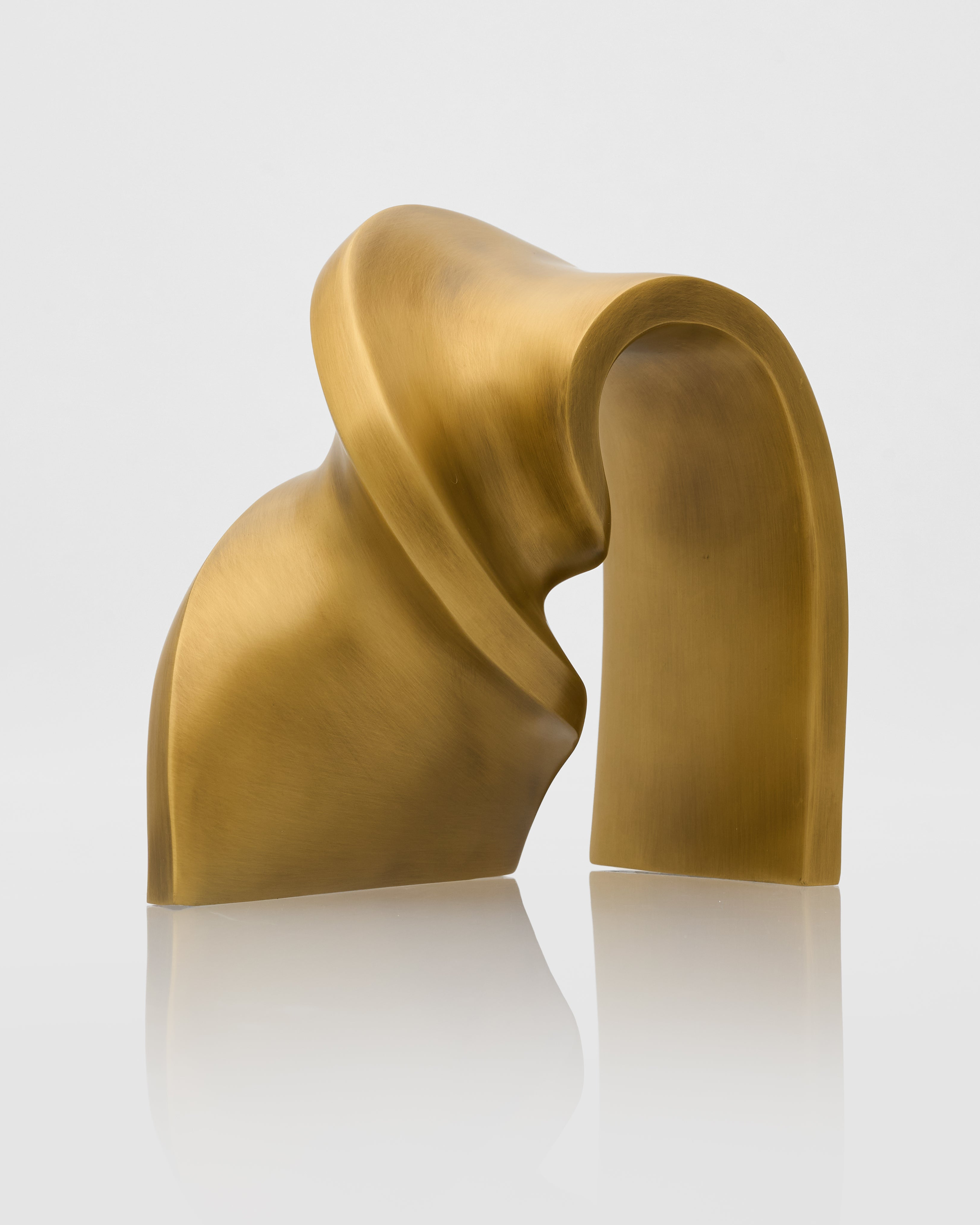 Gold abstract sculpture on a reflective surface with a light gray background