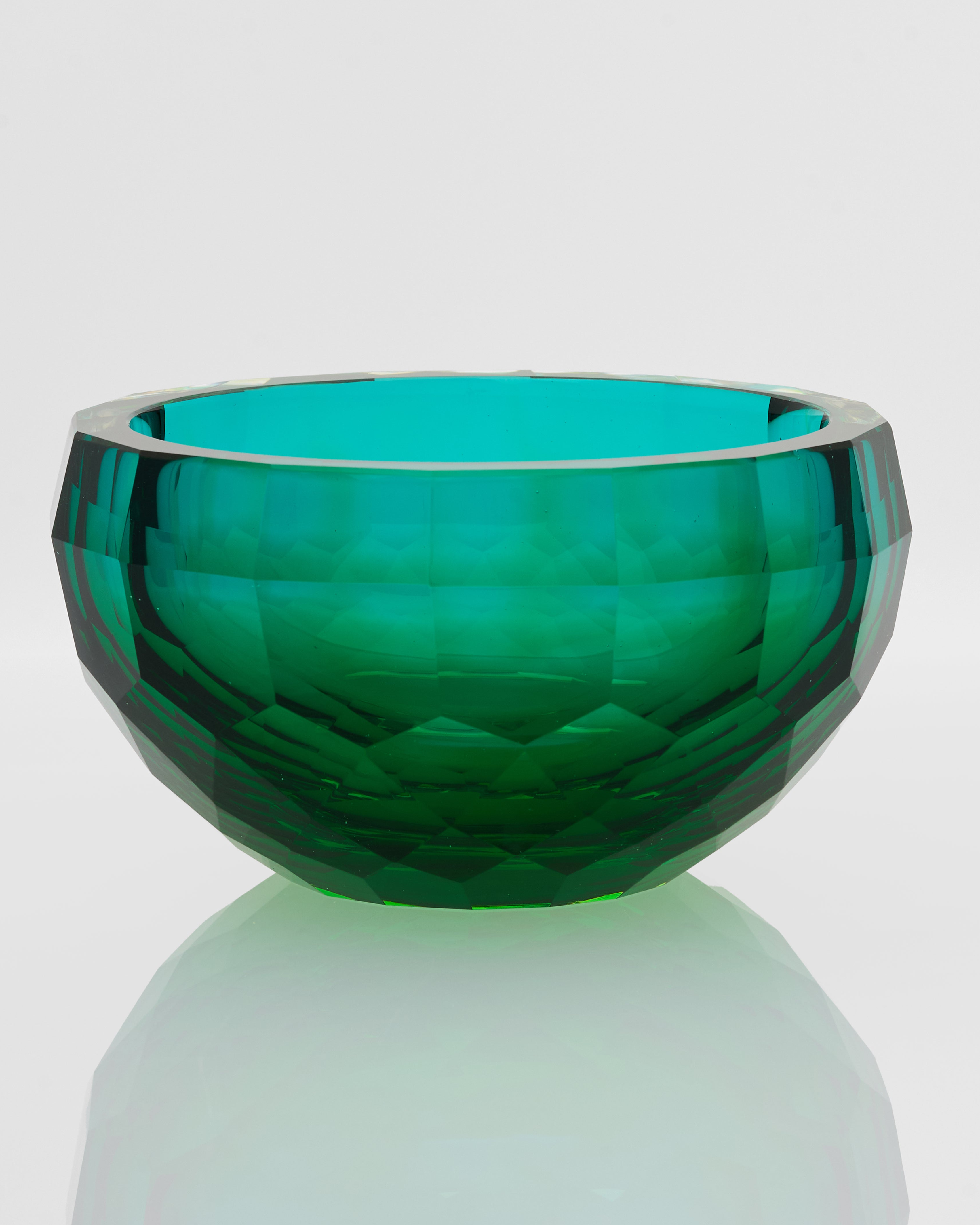 Green glass bowl with faceted design on a light gray background