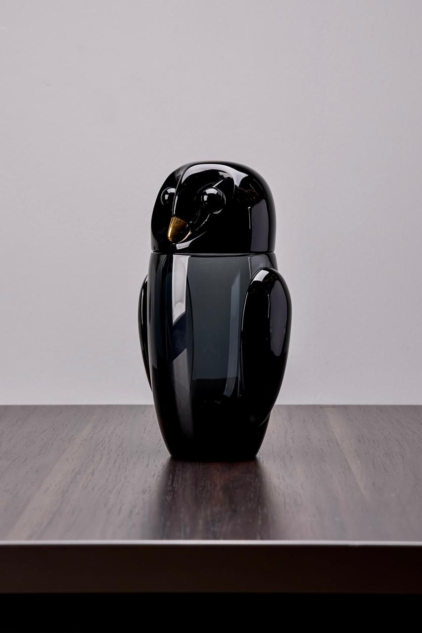 Black owl shaped object on a wooden surface with a gray background