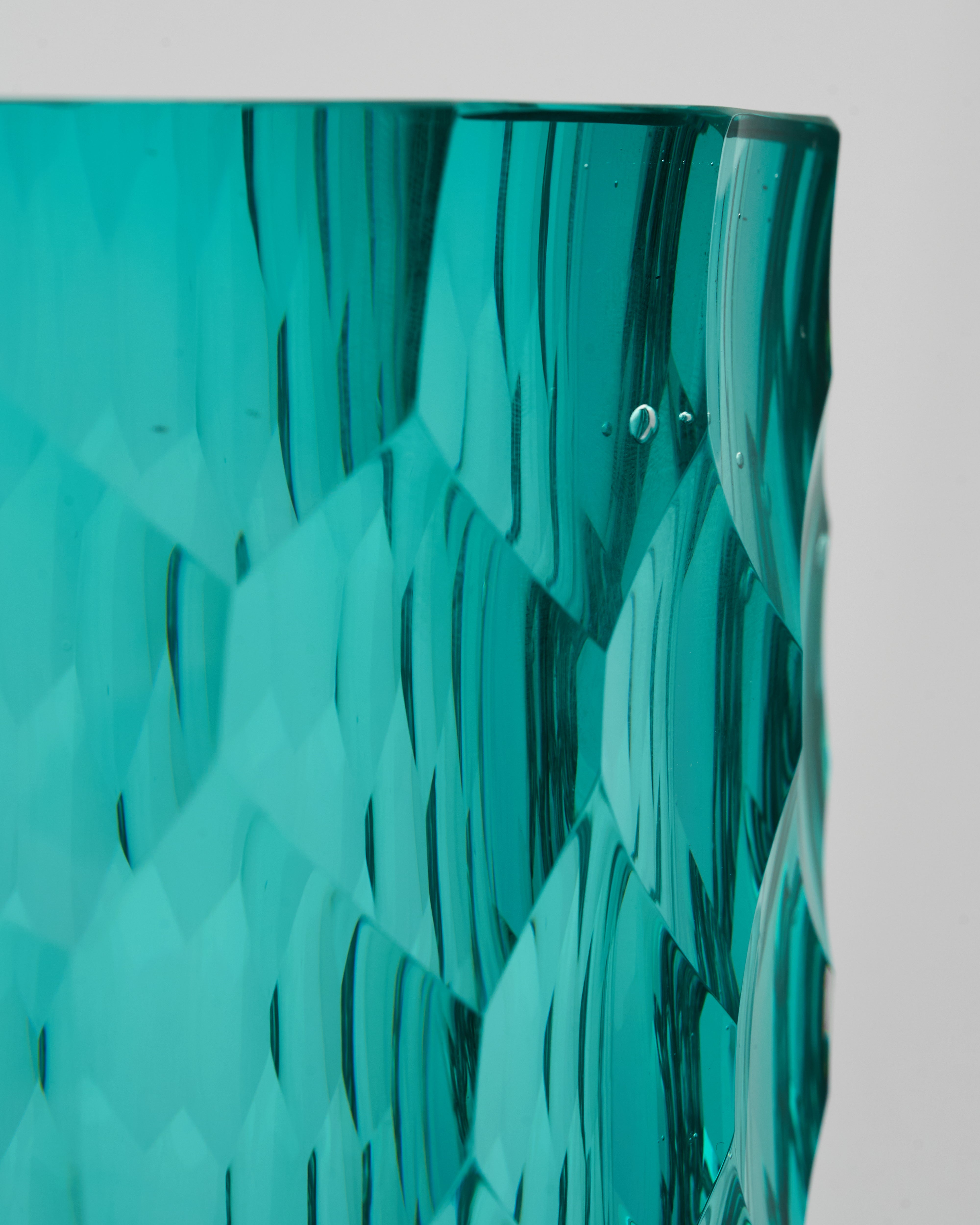 Teal glass vase with textured surface on a light gray background