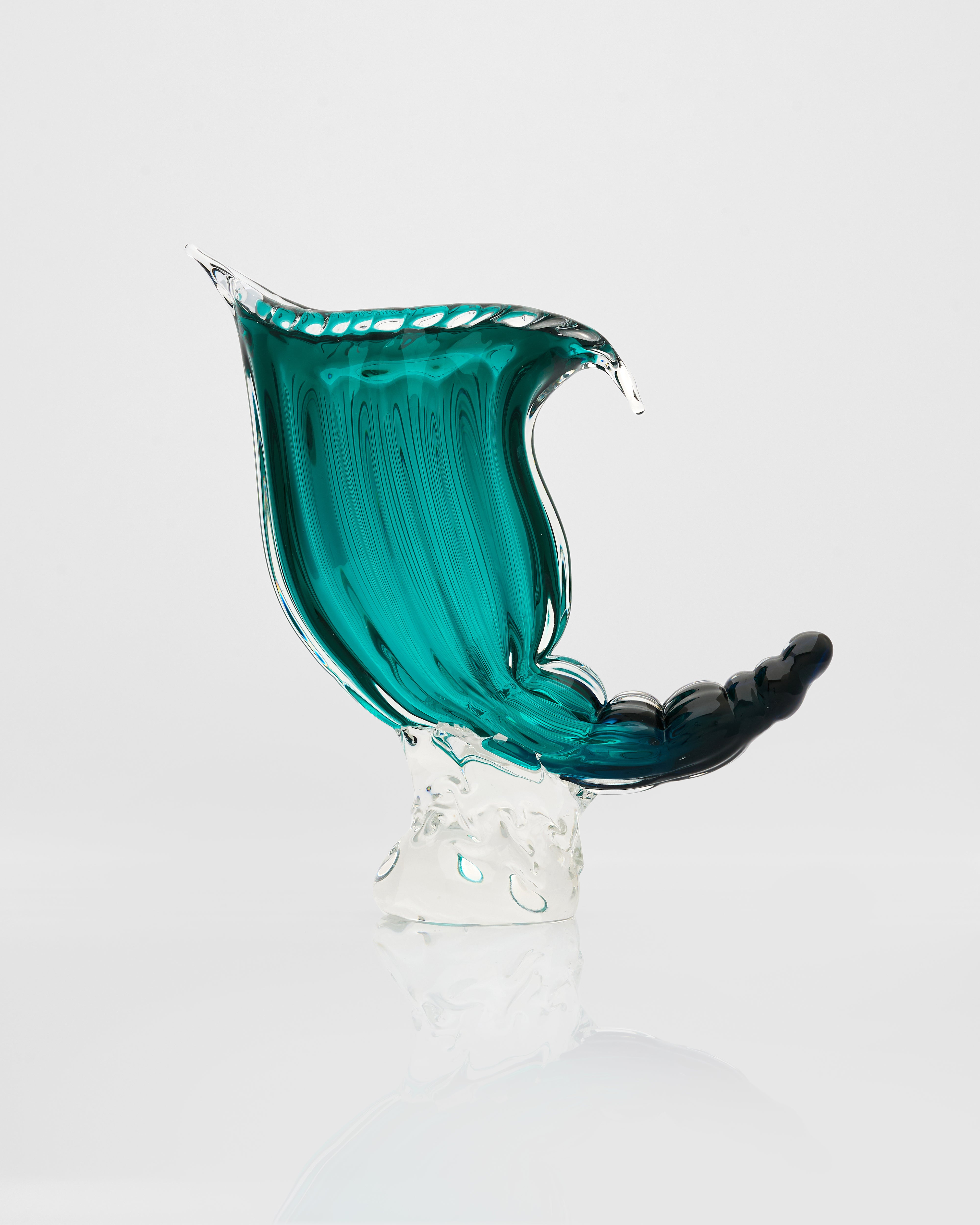 Glass sculpture of a wave with teal and black colors on a white background