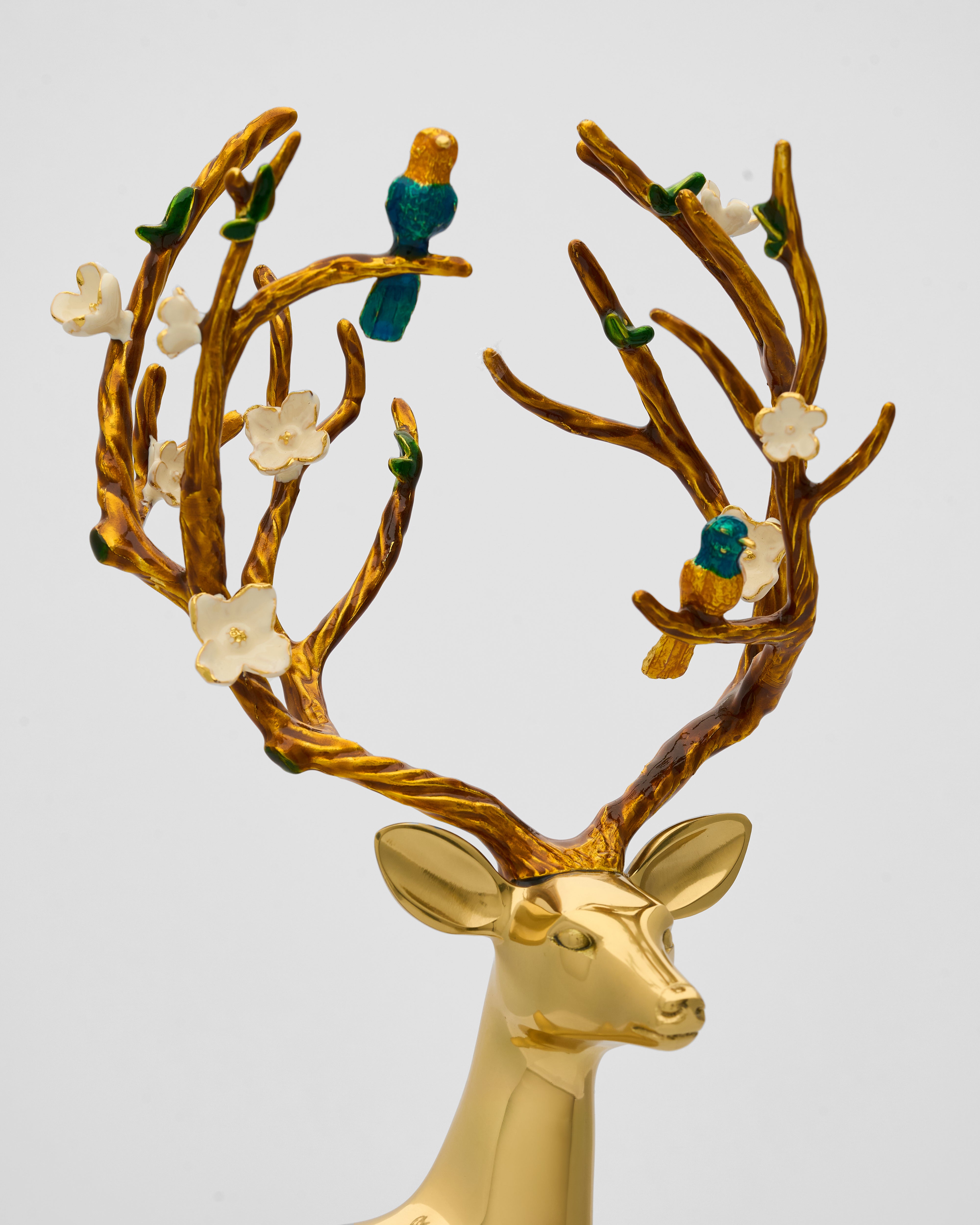 Gold deer head with decorative antlers featuring birds and flowers on a light gray background